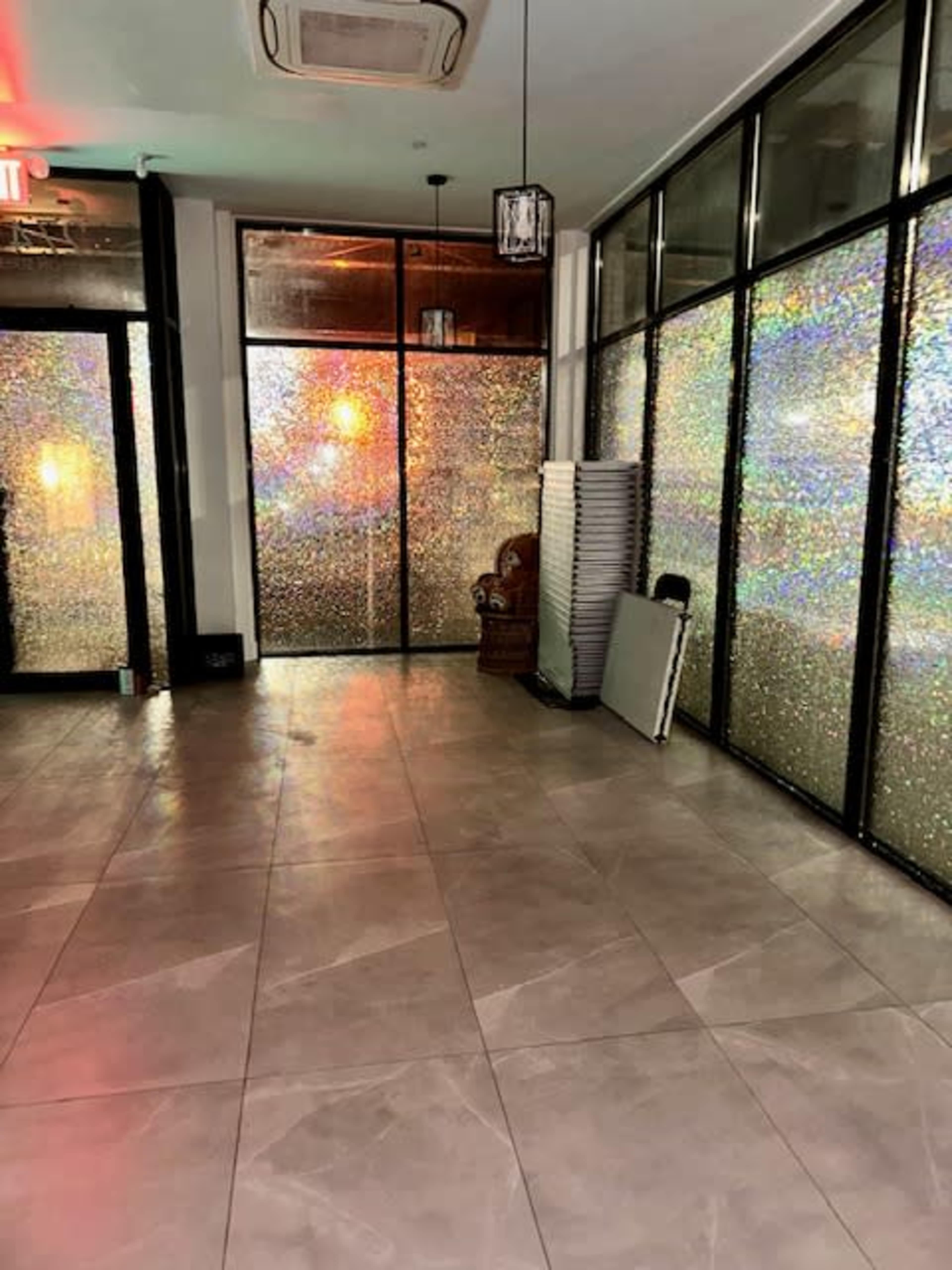 An empty interior space with glass walls featuring reflective surfaces and a corner with stacked folding chairs.