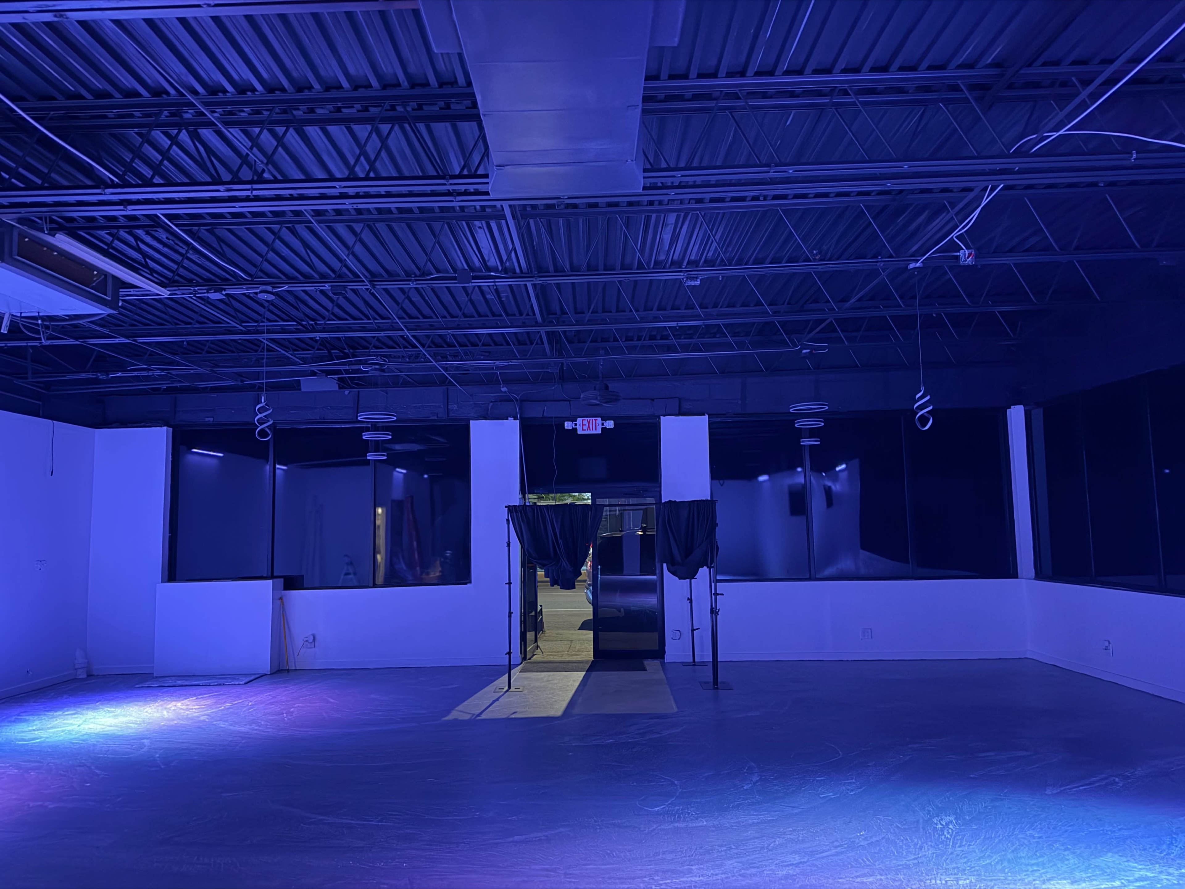 The image shows an empty interior space with dark walls and blue lighting, featuring a doorway framed by black curtains.