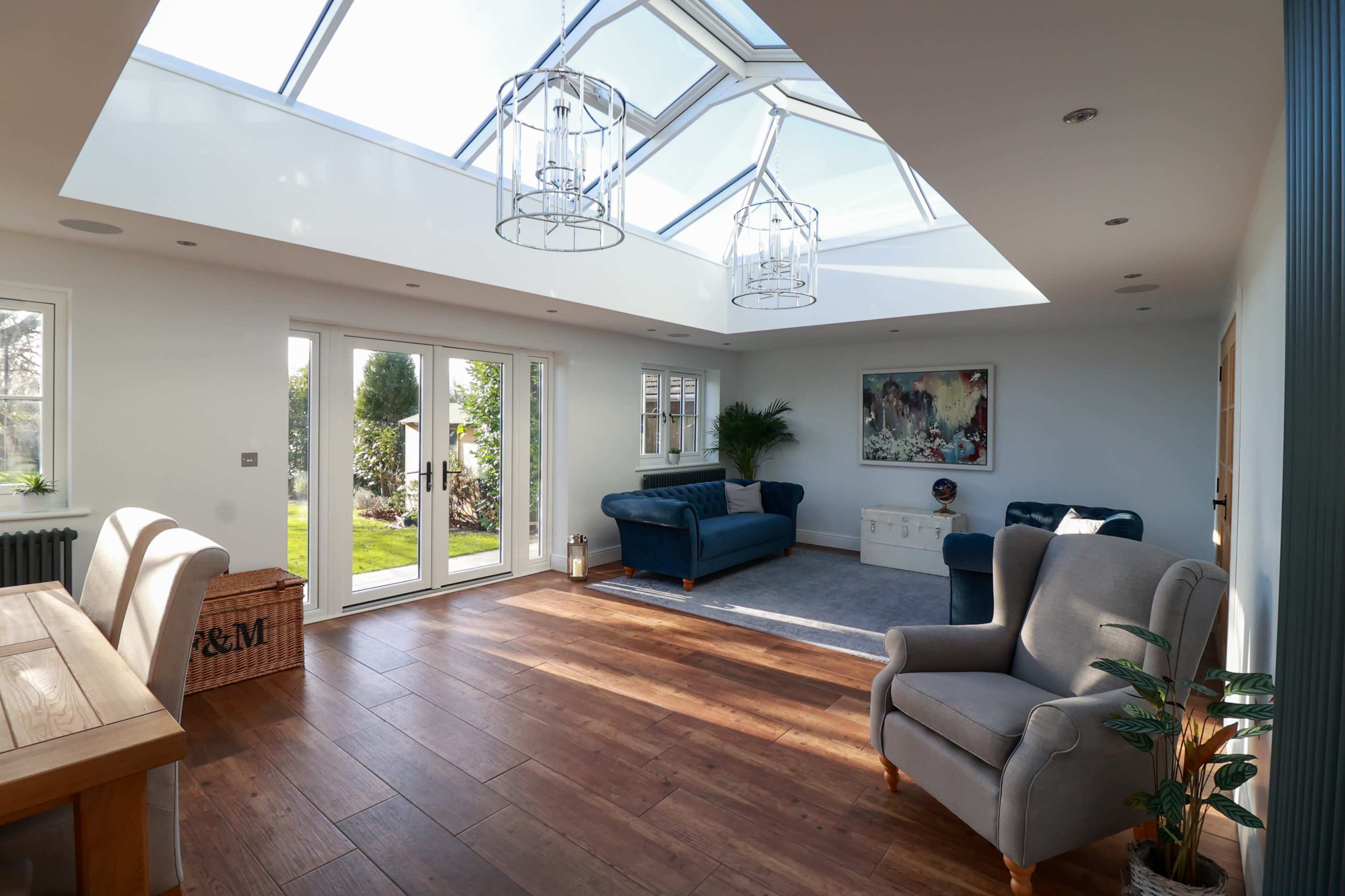A bright living room features large glass panels in the ceiling, modern furniture, and opens to a garden through double doors.