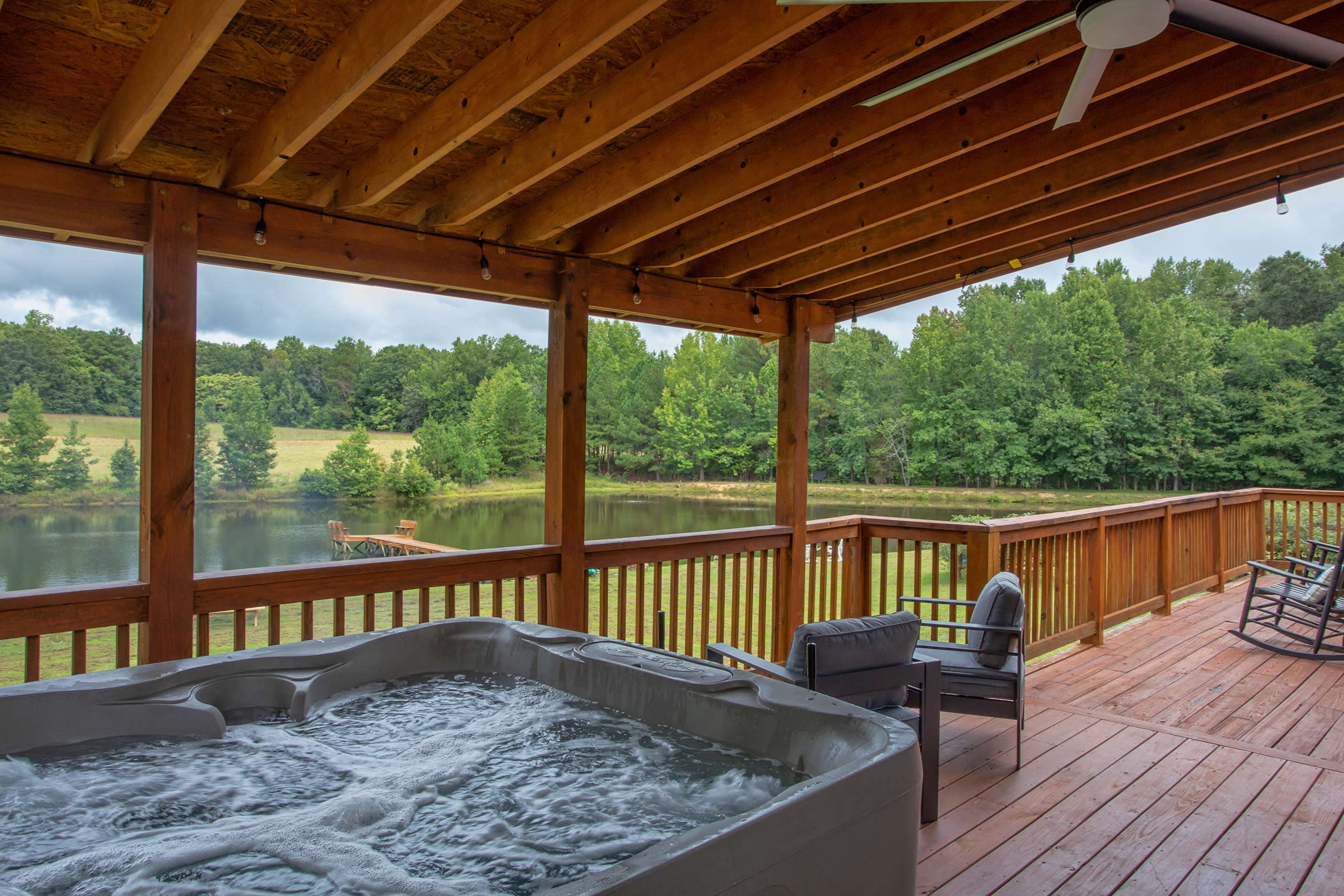 A hot tub is positioned on a wooden deck overlooking a tranquil pond surrounded by trees.