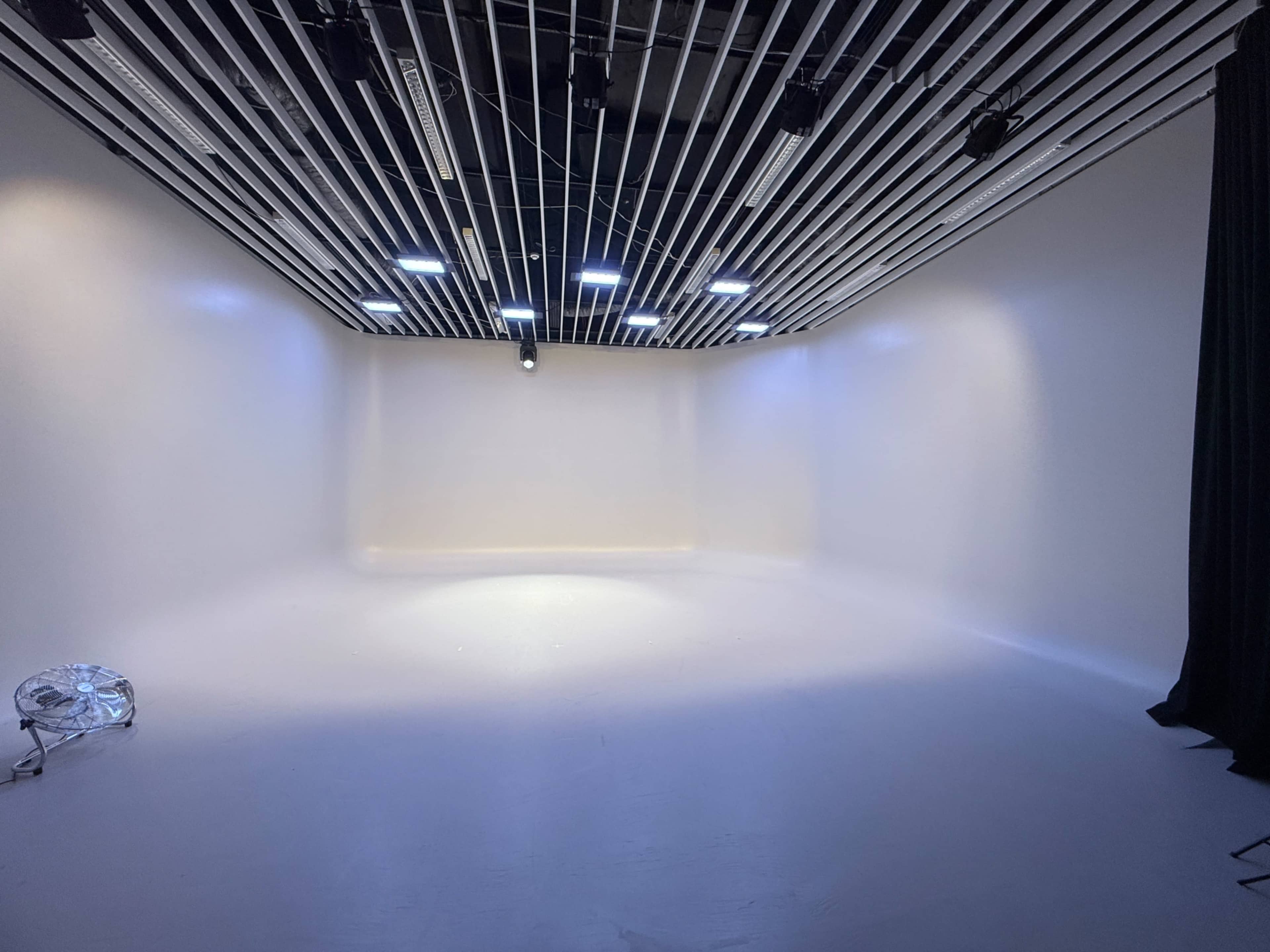 The image shows an empty studio space with white walls, a smooth floor, and overhead lighting.