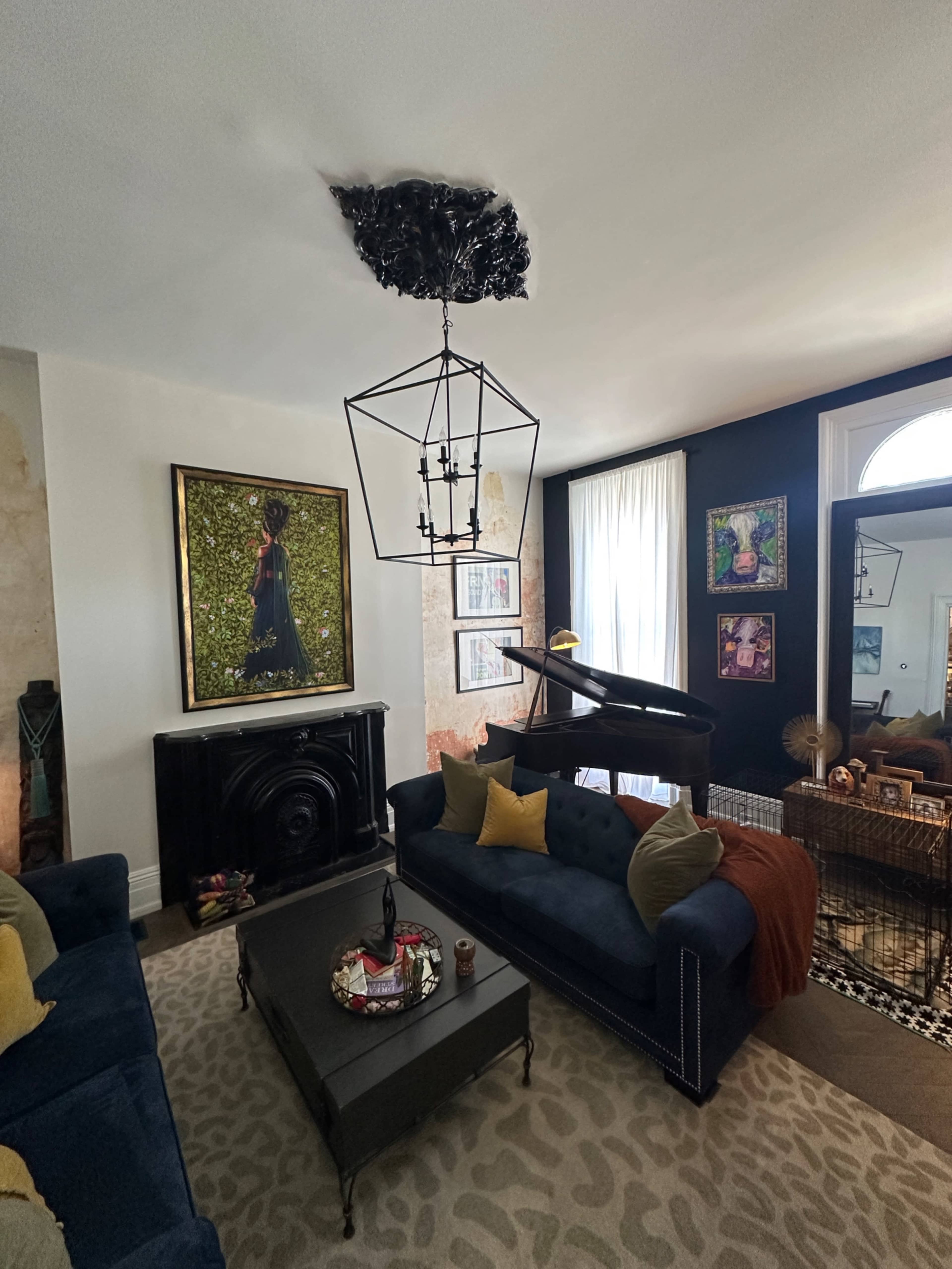 The image shows a stylish living room with dark blue sofas, a coffee table in the center, and a decorative hanging light fixture above, along with artwork on the walls.