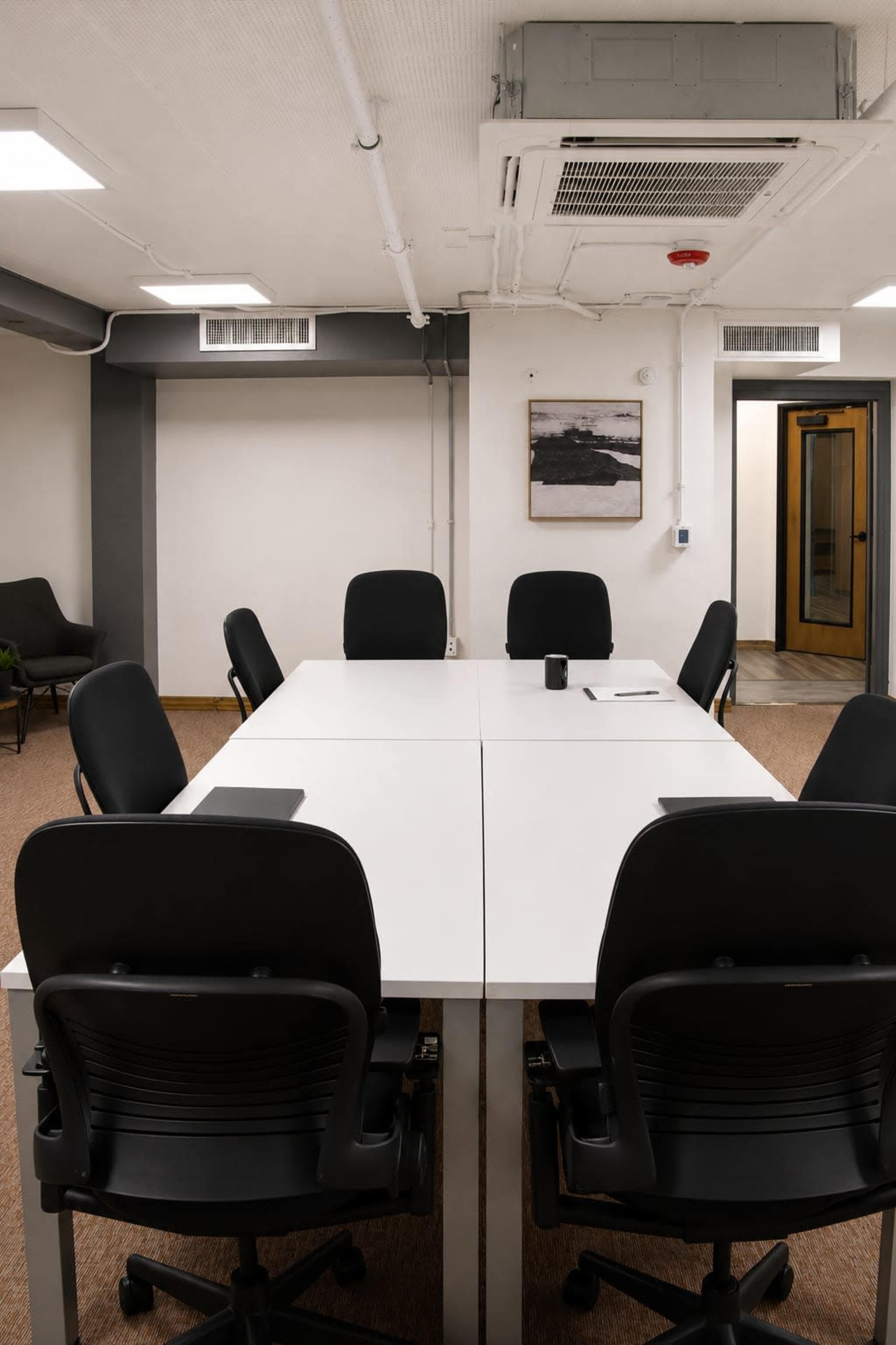 A large, modern conference room features a long white table surrounded by black chairs, with a door and a piece of wall art visible in the background.