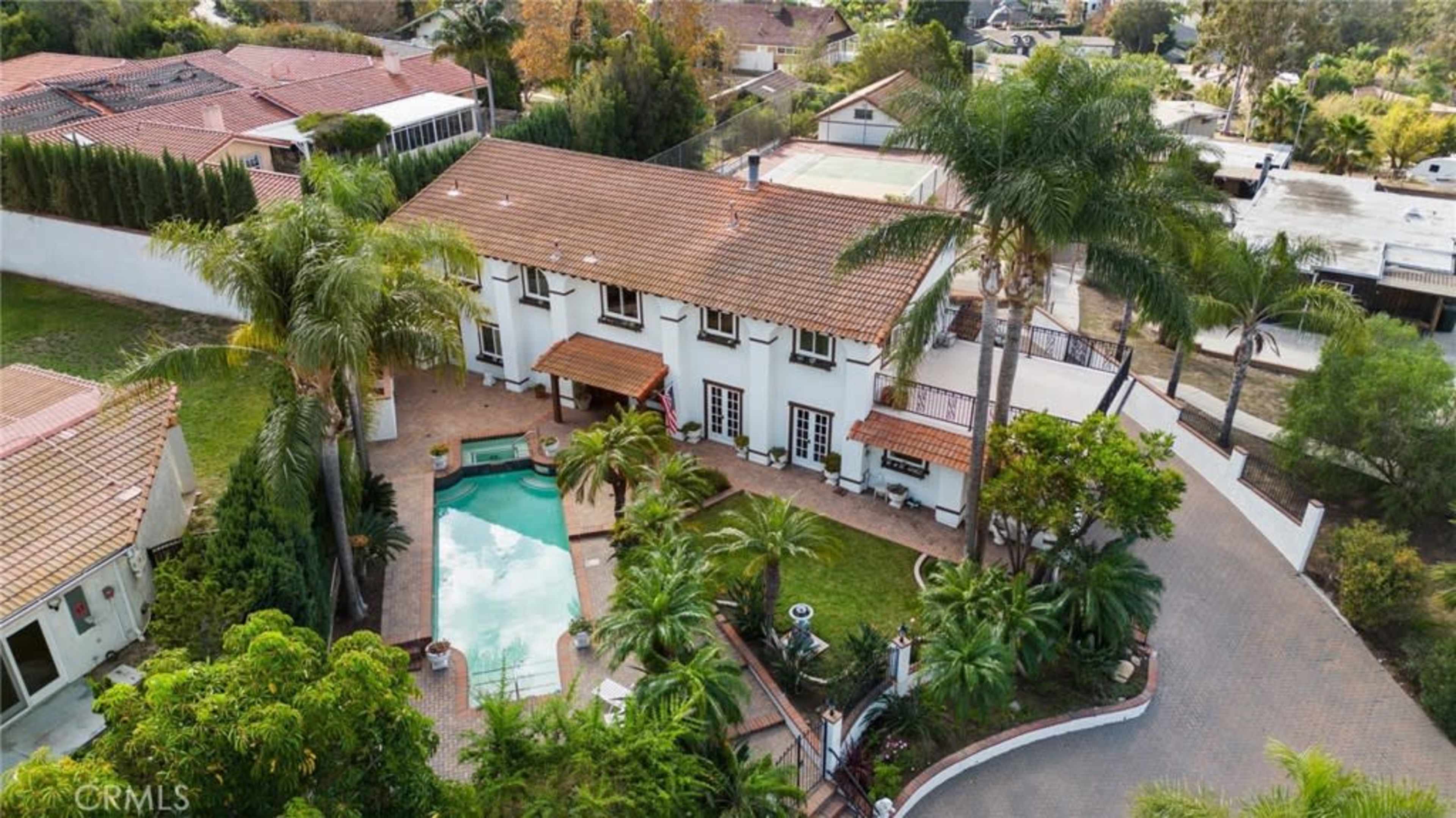 The image shows a two-story house with a terracotta tile roof, a swimming pool in the backyard, and surrounding palm trees and landscaped greenery.