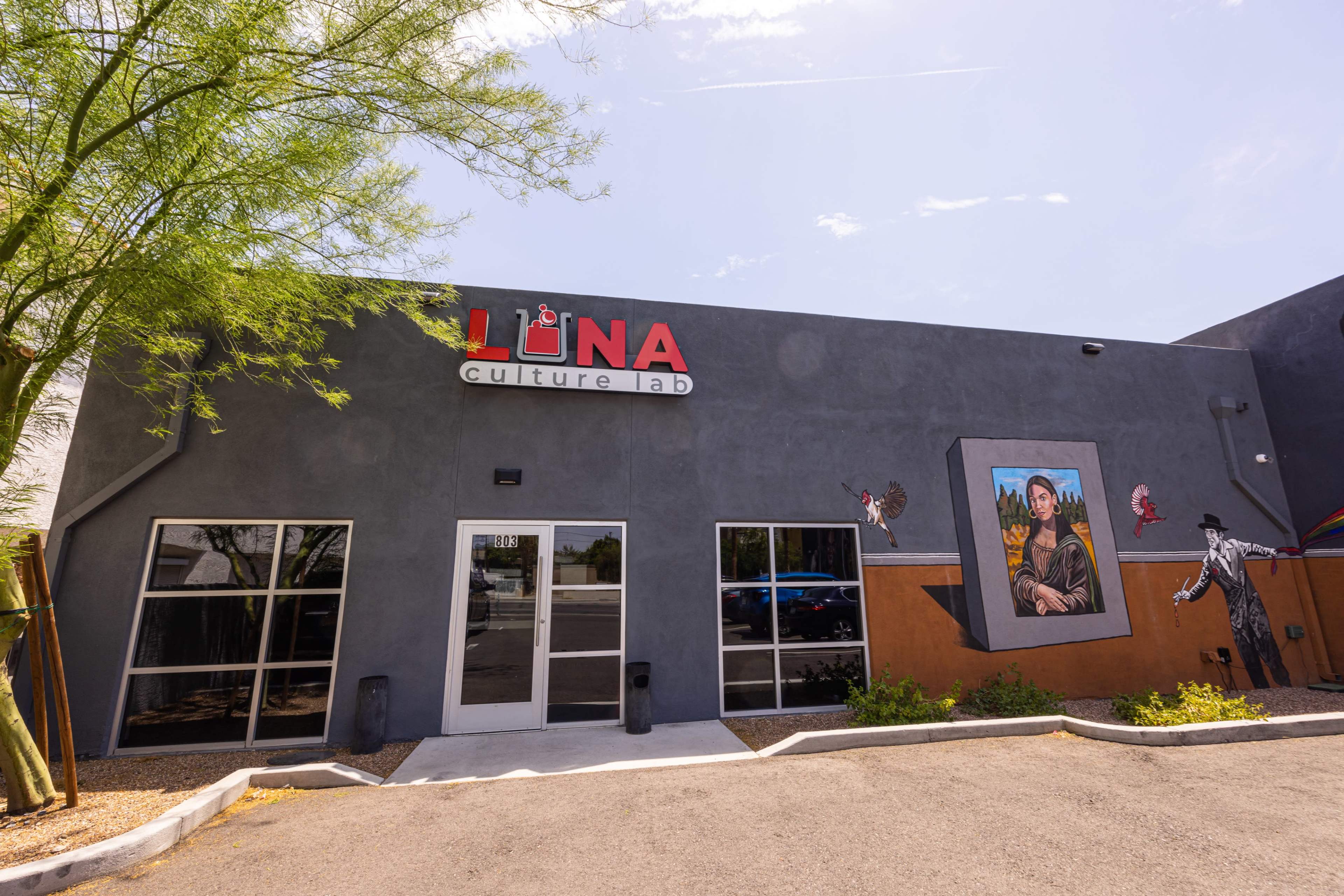 A gray building with large glass entrances features the sign "Luna Culture Lab" and has a mural on the side depicting a figure with a crown.