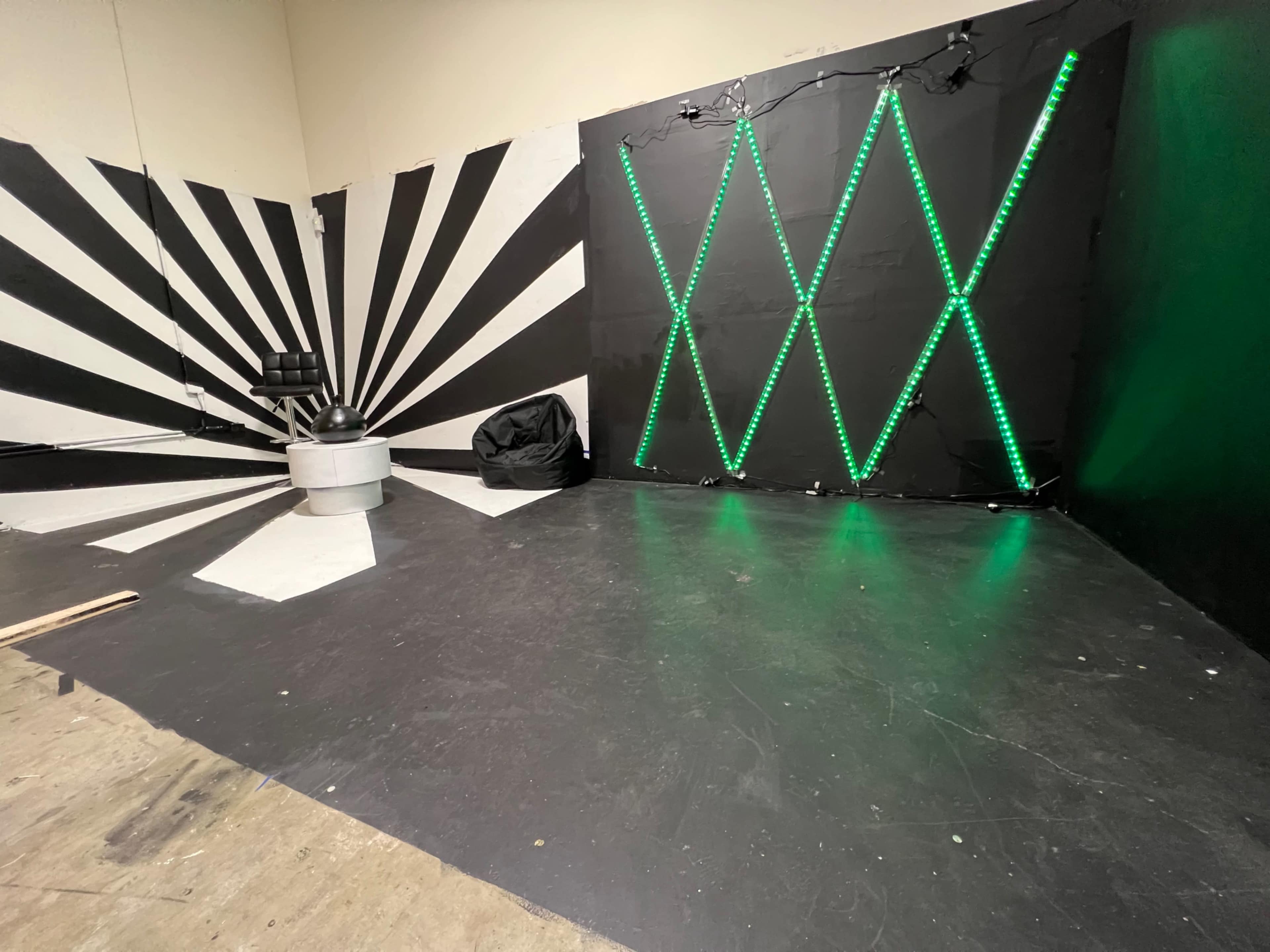 A room with a black and white striped wall, a chair, and a backdrop featuring green LED lights arranged in a crisscross pattern.