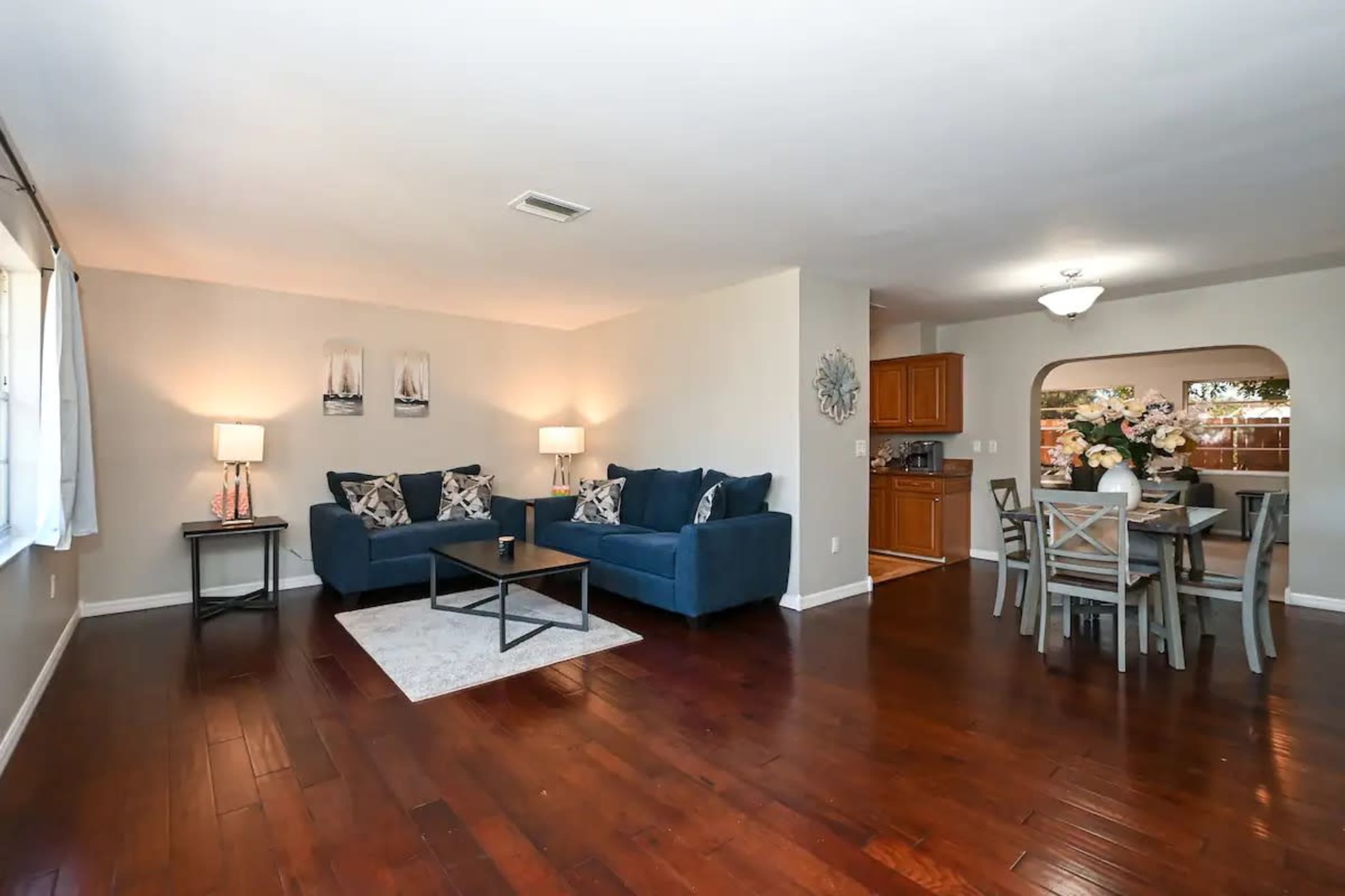 A living room with a blue sectional sofa, a coffee table, and a dining area featuring a table and chairs, all set against a backdrop of hardwood floors and warm lighting.