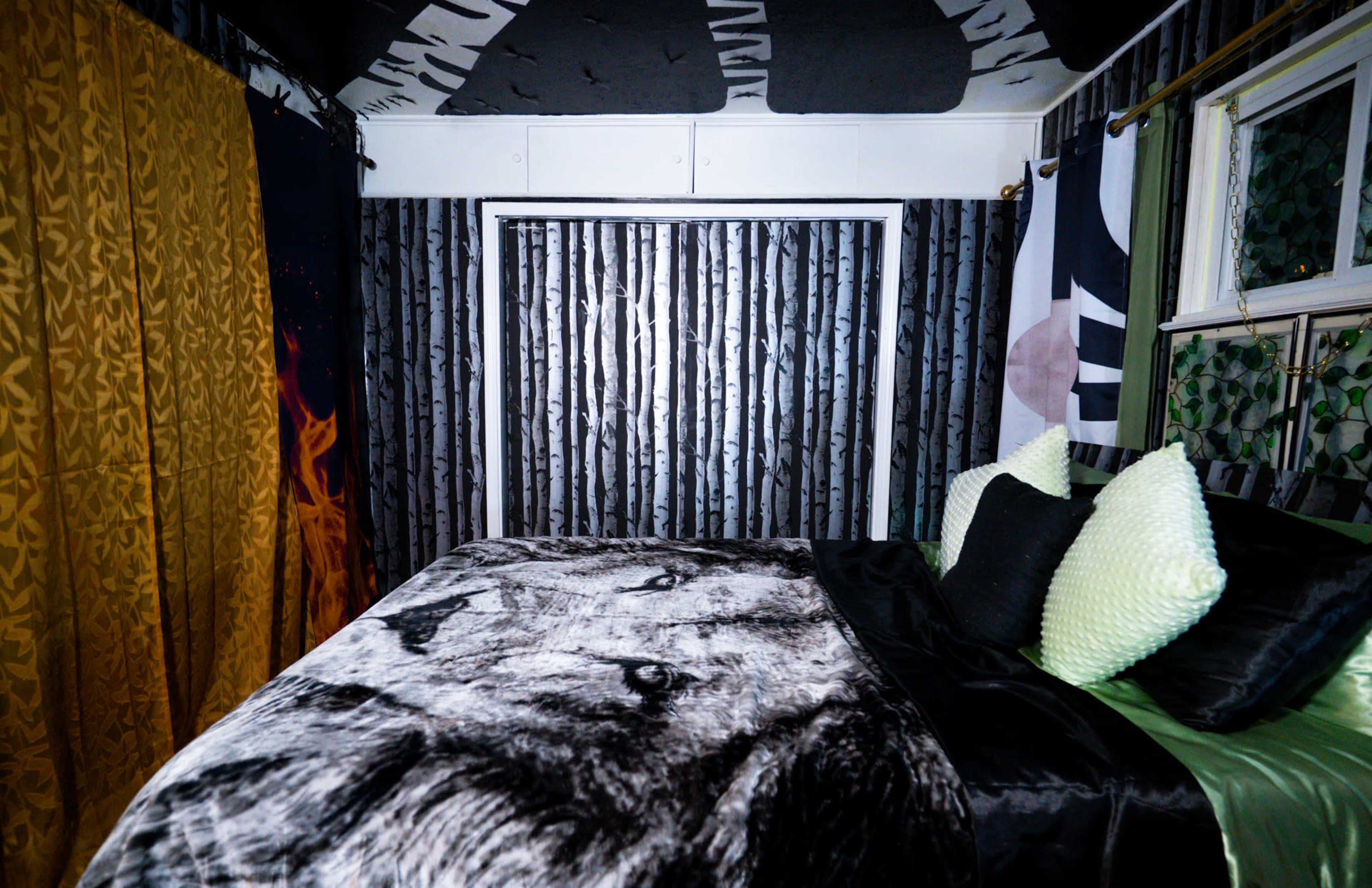 The image shows a bedroom with a black and white lion blanket on the bed, surrounded by dark patterned walls and golden curtains.