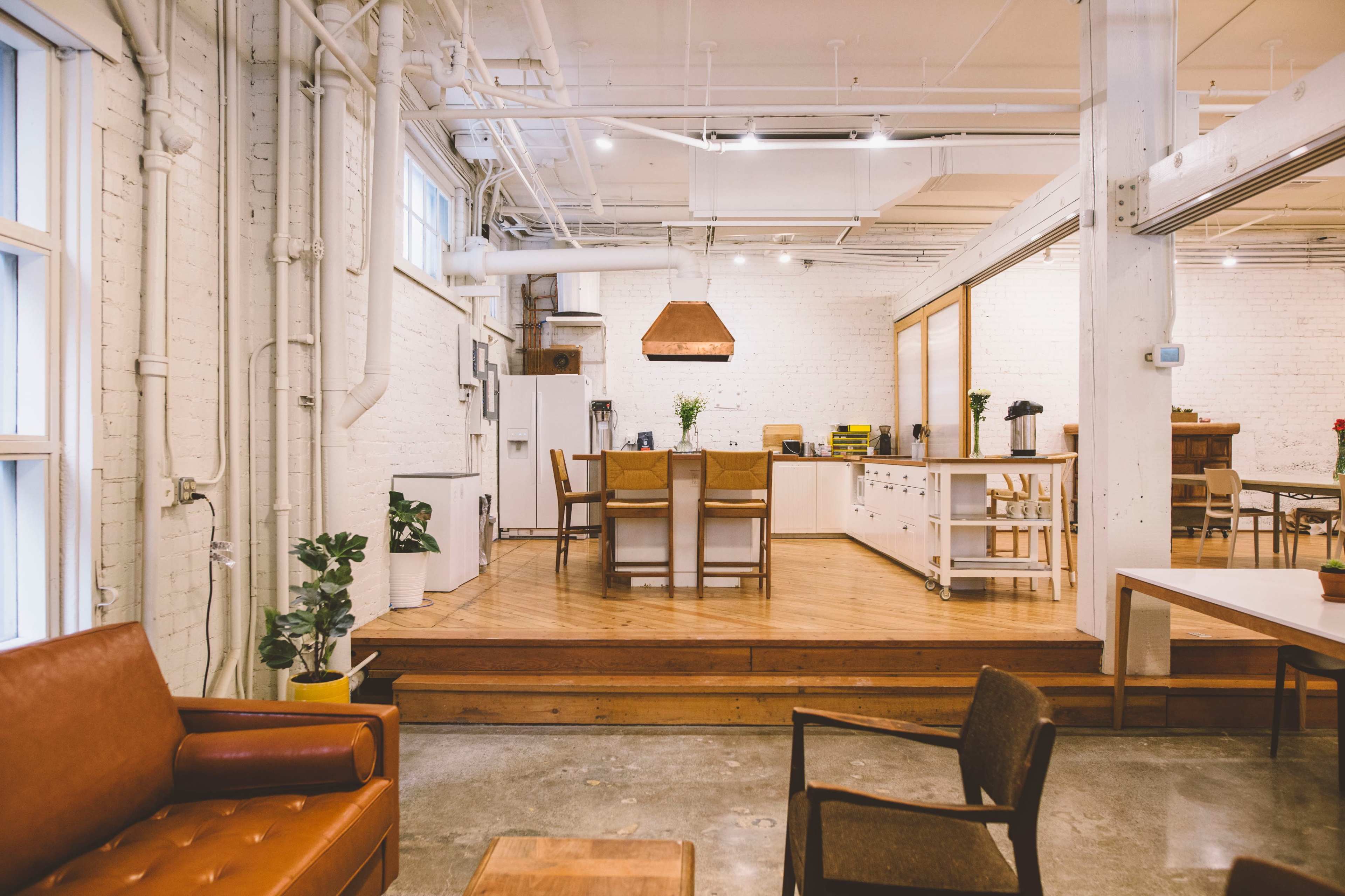 A spacious kitchen and dining area with wooden floors, modern furniture, and industrial-style lighting.