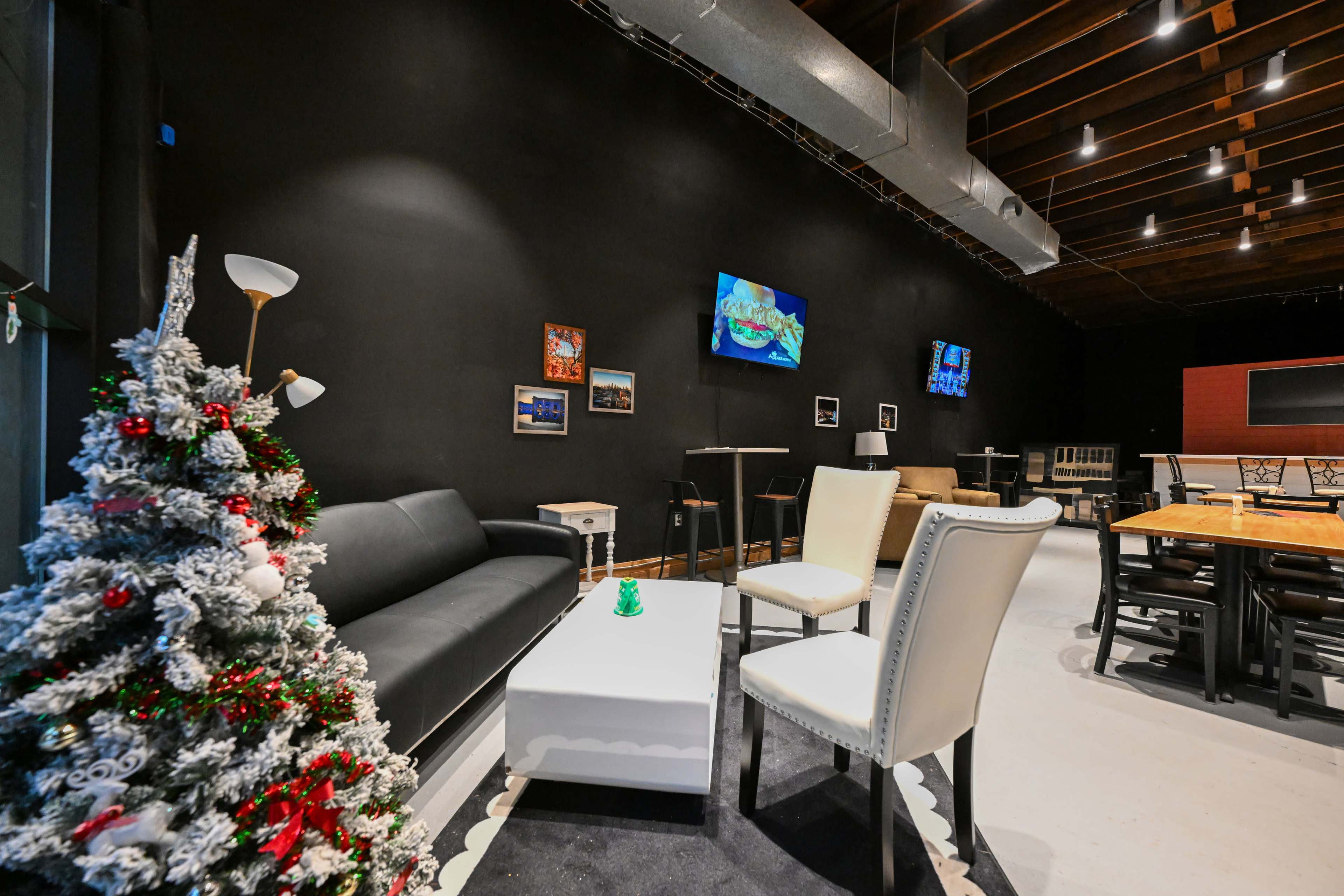 The scene features a modern lounge area with black walls, a decorative Christmas tree, a white coffee table, seating, and flat-screen TVs mounted on the walls.