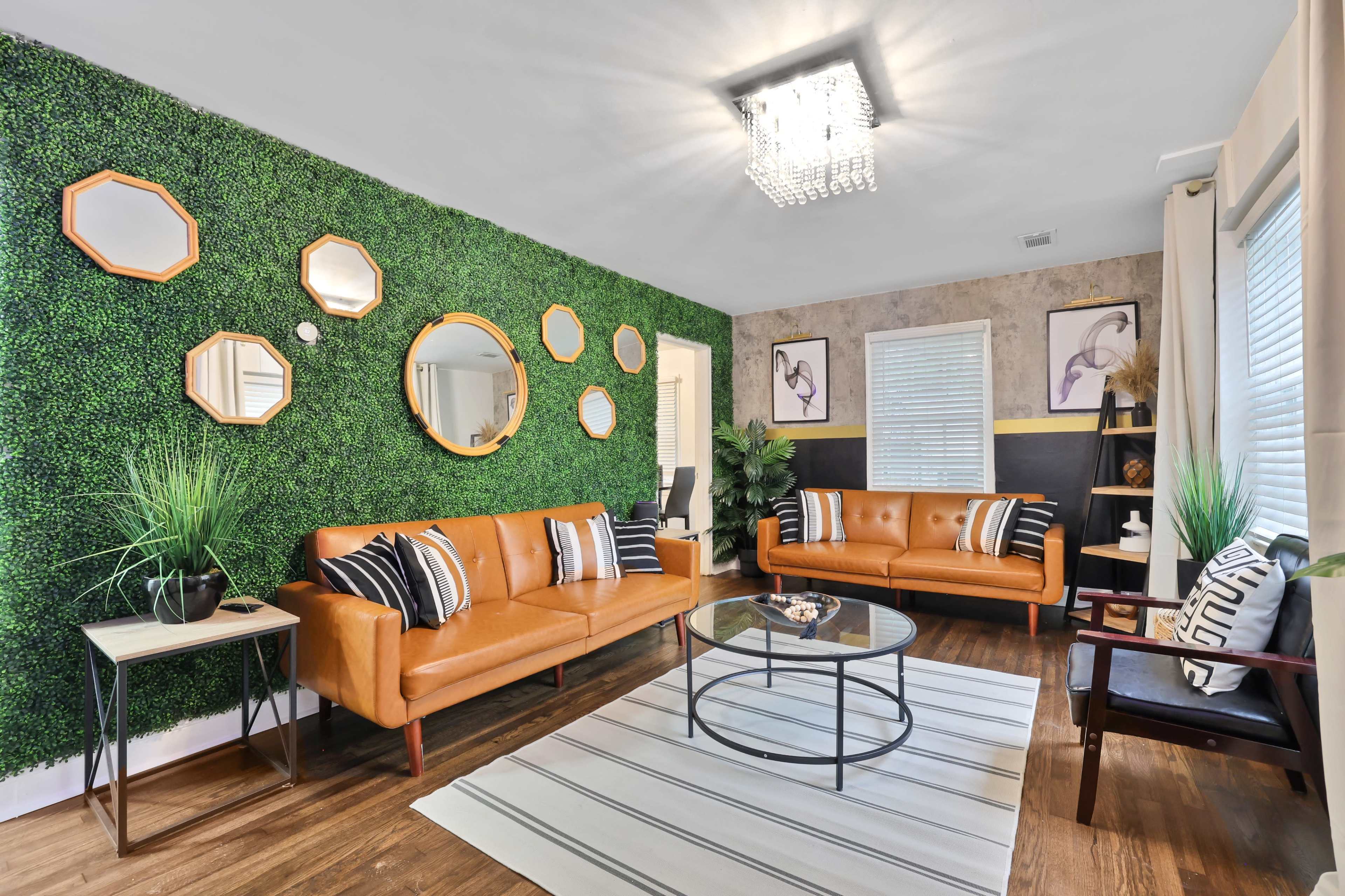 The room features two brown leather sofas, a glass coffee table, and a green wall adorned with round mirrors and decorative plants.