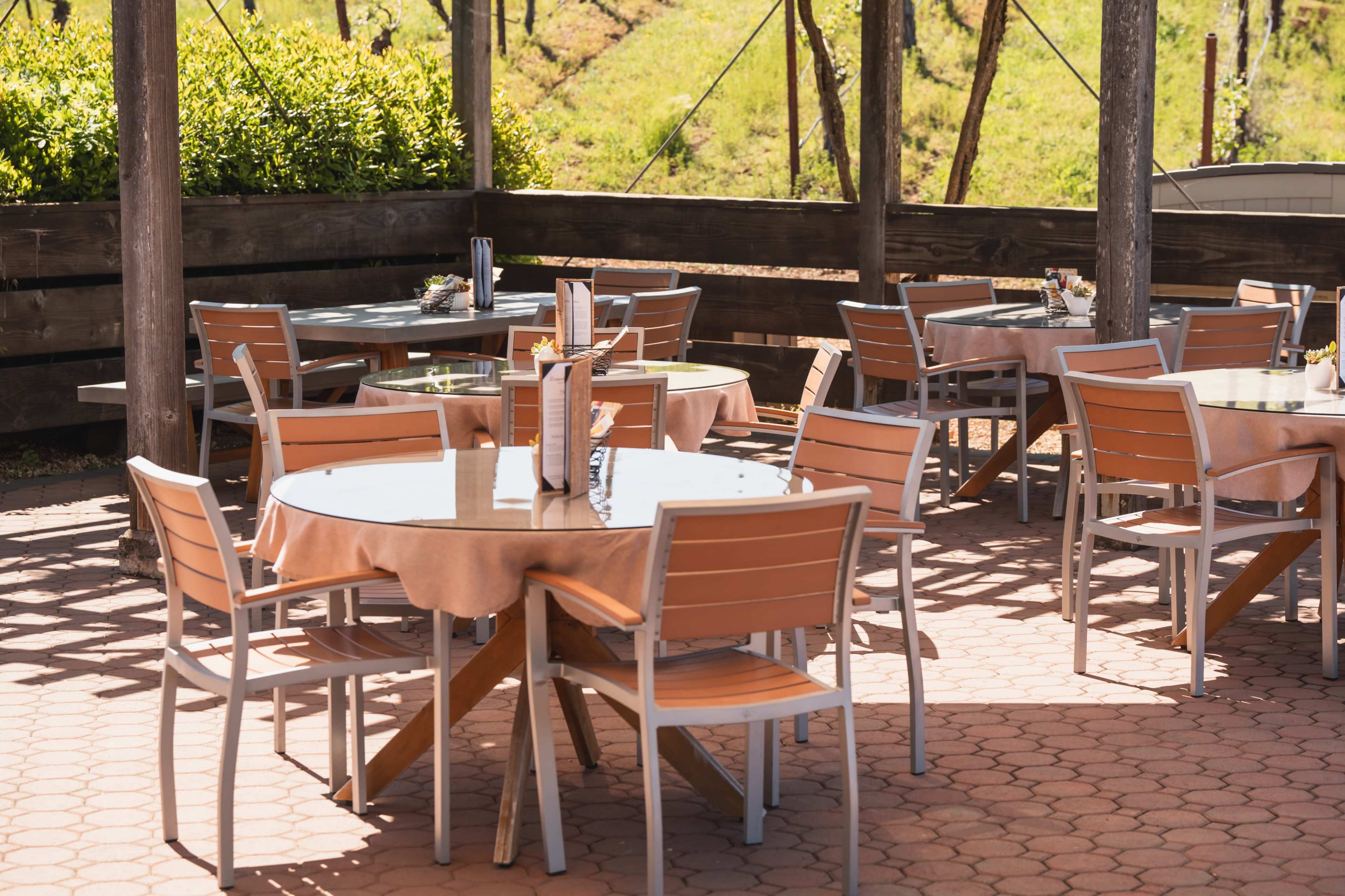 The image shows a series of empty tables set outside under a wooden overhang in a restaurant setting.
