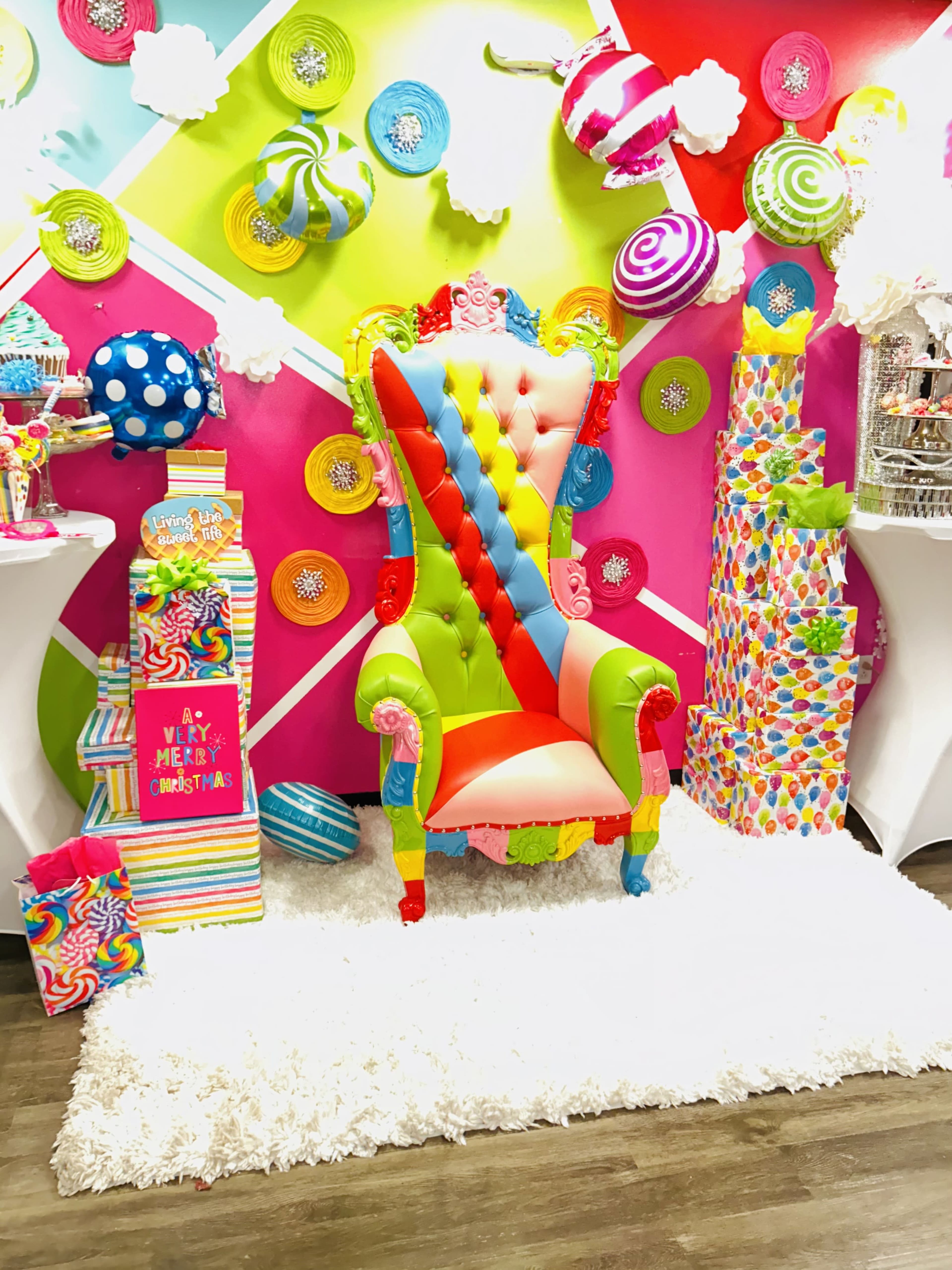 A brightly colored, whimsical chair placed in front of a vibrant backdrop decorated with oversized candy-themed decorations.