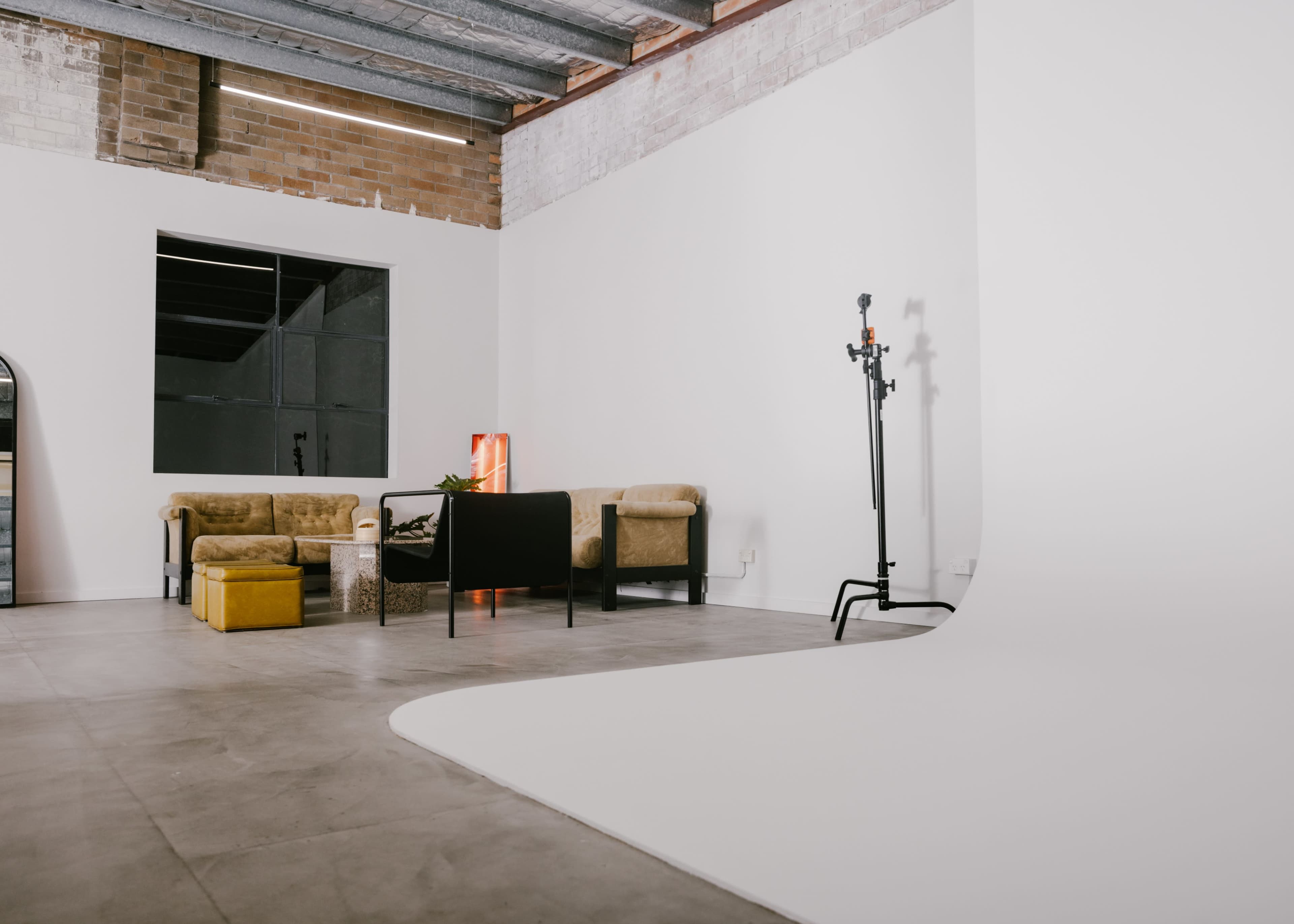 A spacious, minimalist room with a seating area featuring a sofa, a coffee table, and a yellow ottoman, alongside a backdrop for photography.