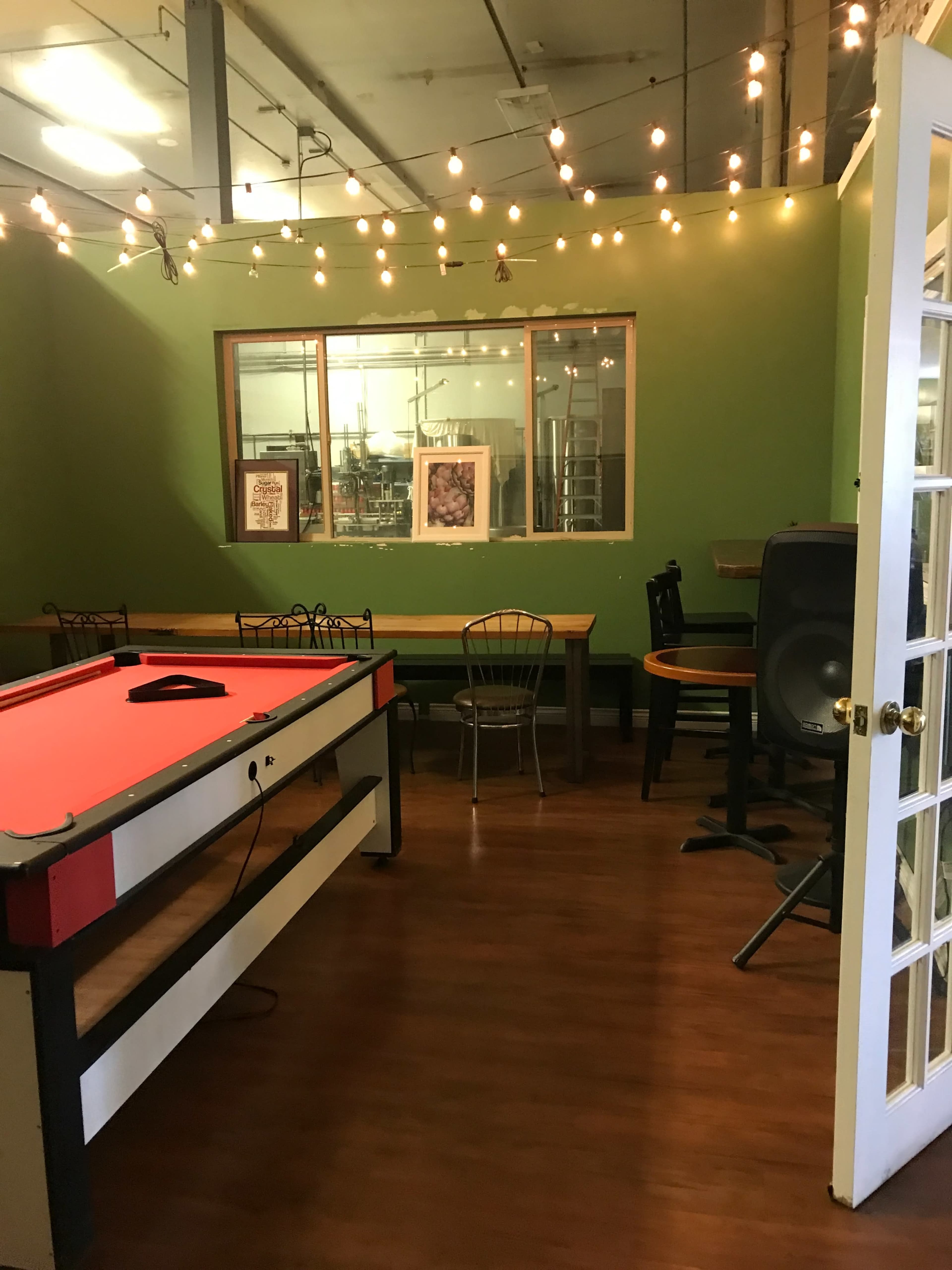 A recreational room with a red air hockey table, surrounded by various tables and chairs, and illuminated by string lights on the ceiling.