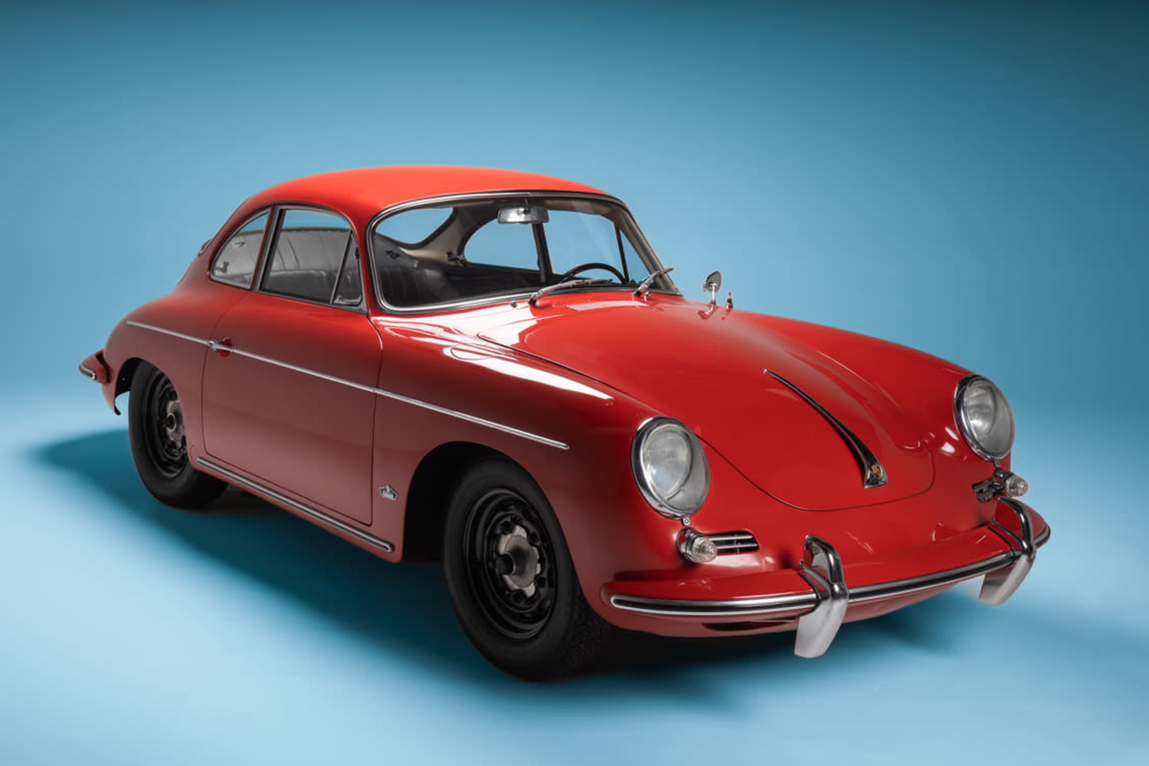 A red vintage Porsche 356 is displayed against a light blue backdrop.