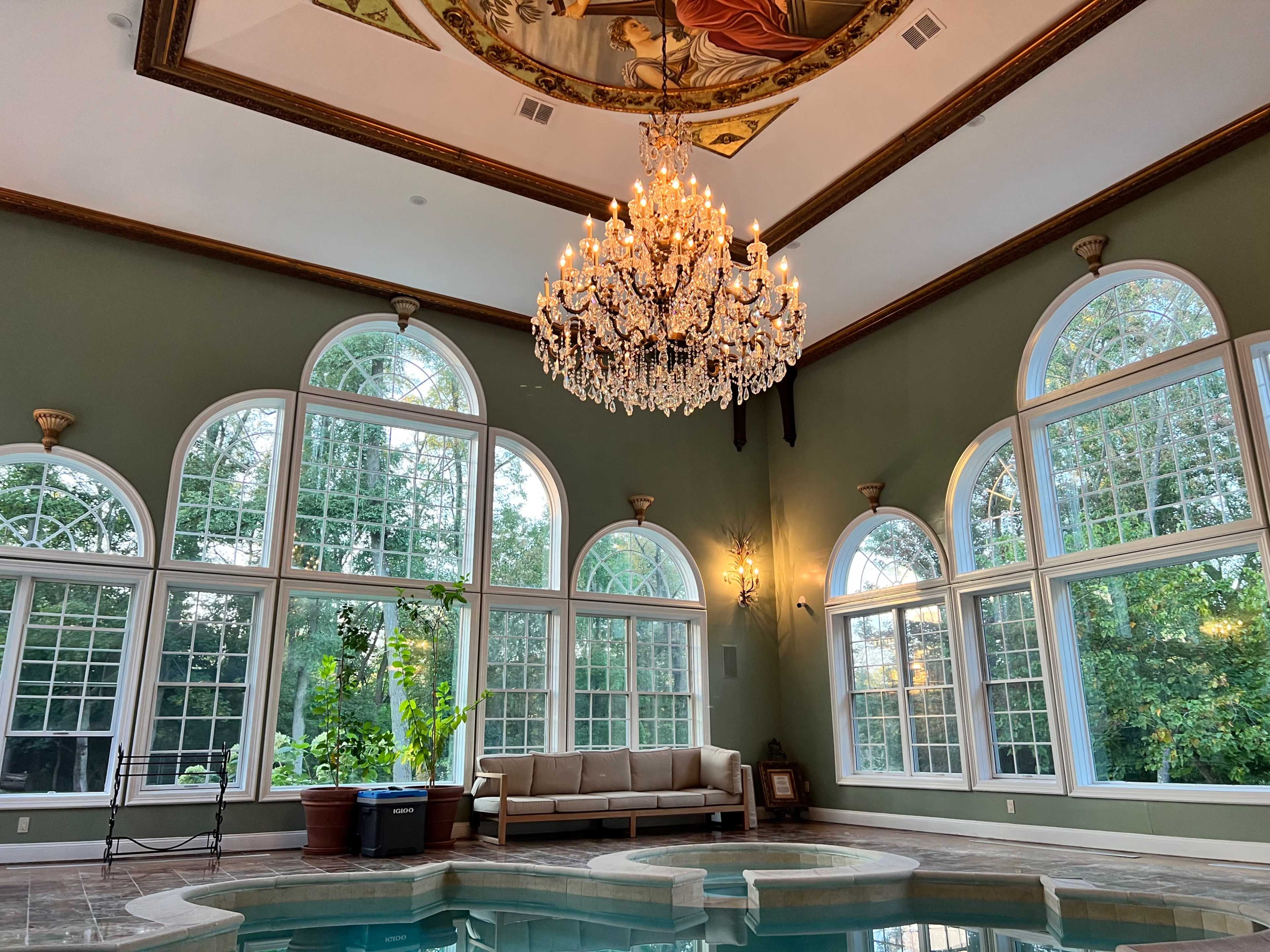 The scene features a well-lit indoor pool area with large arched windows, a chandelier, and a mural on the ceiling.