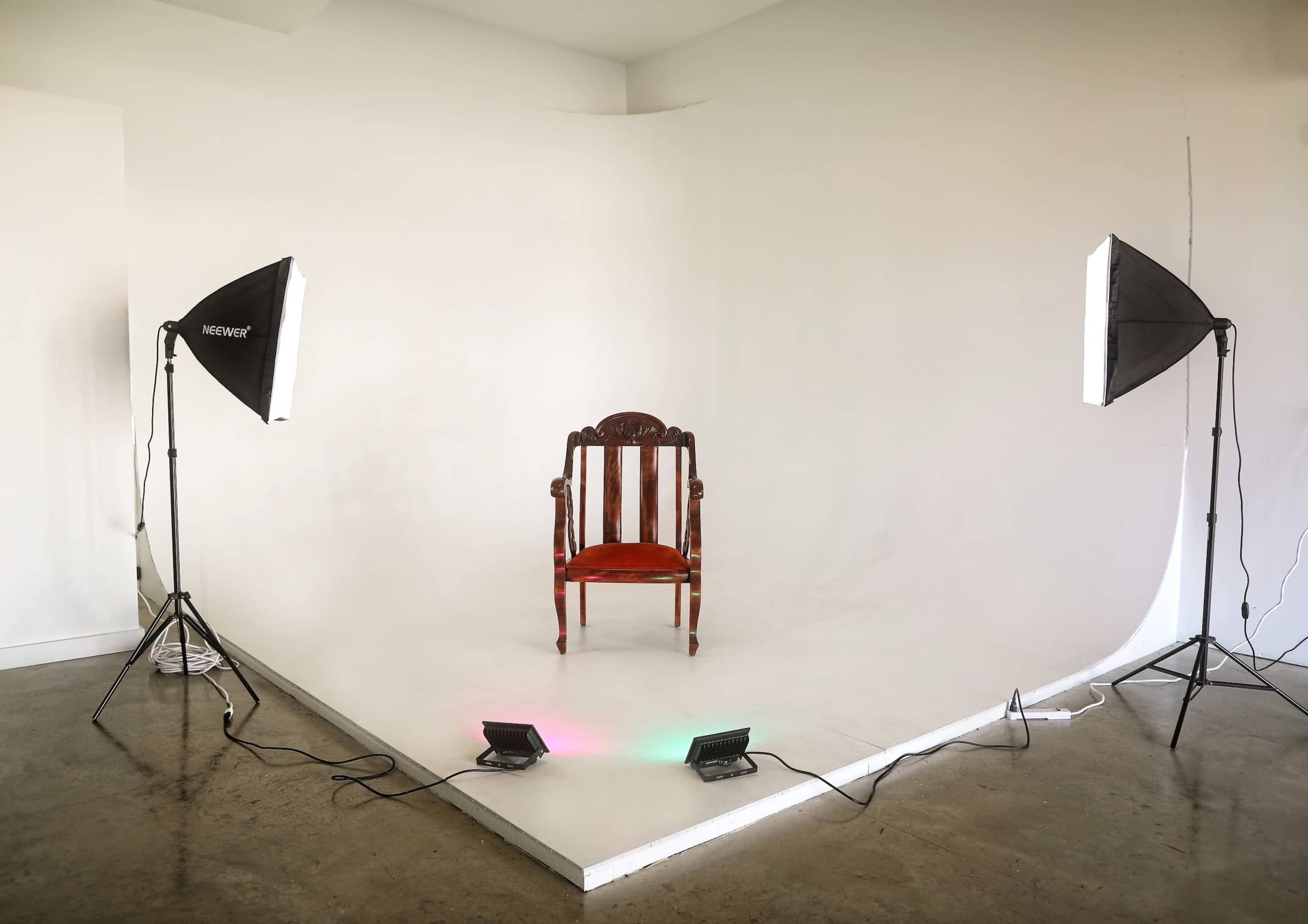 A red chair is positioned in the center of a well-lit studio with two softbox lights on either side.