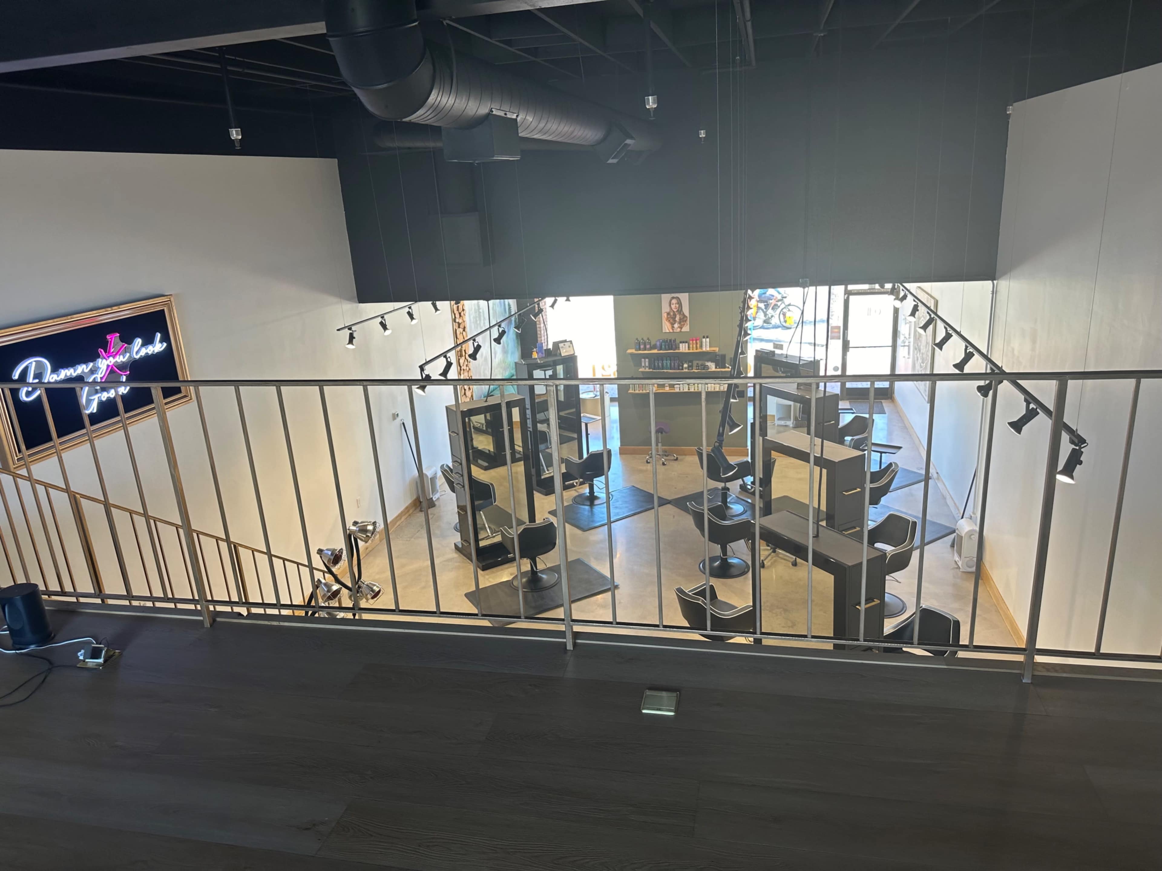 The image shows an elevated view of a hair salon featuring several styling stations, black chairs, and bright lighting.