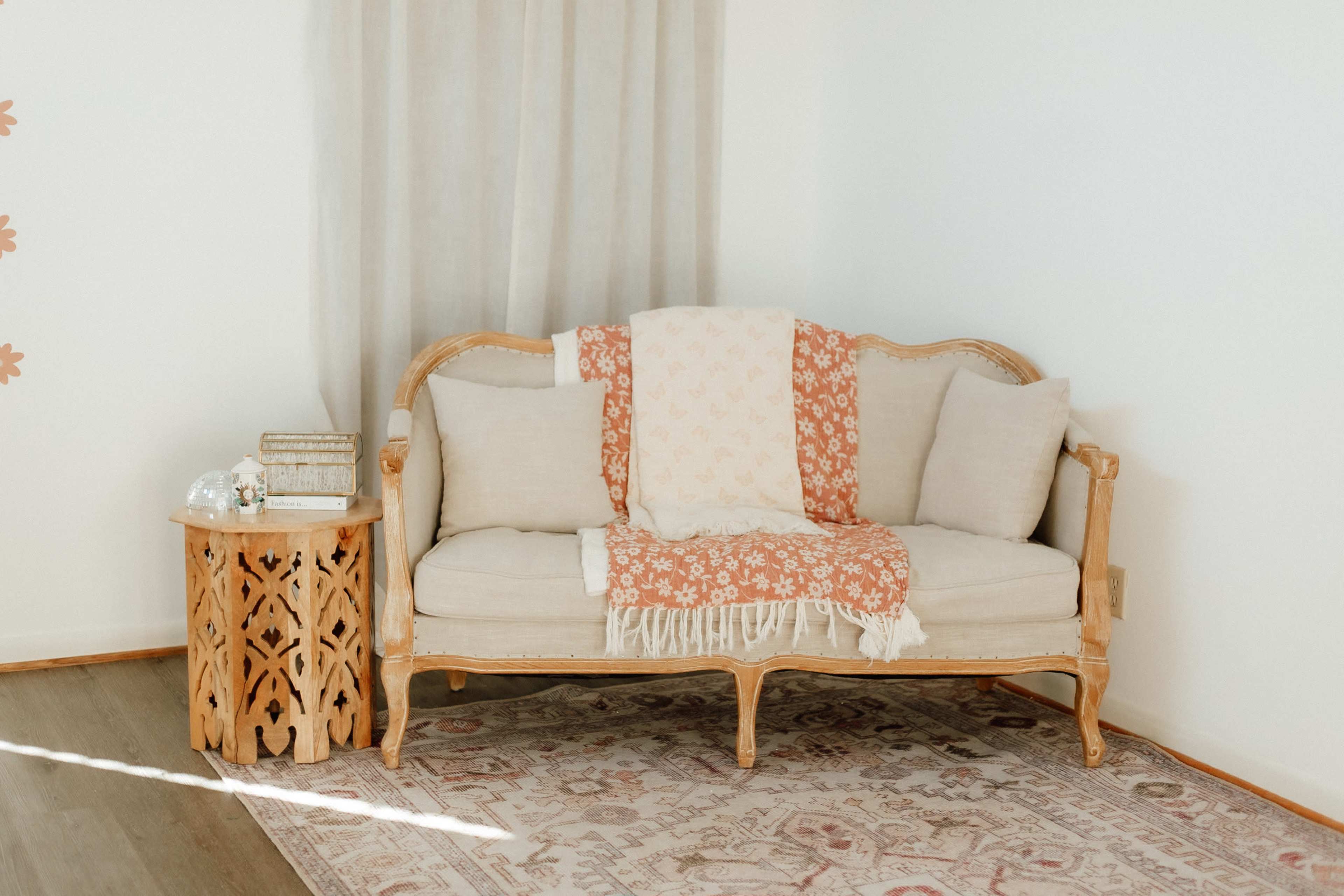 A vintage-style wooden sofa with light cushions is placed next to a carved wooden side table and a patterned rug.
