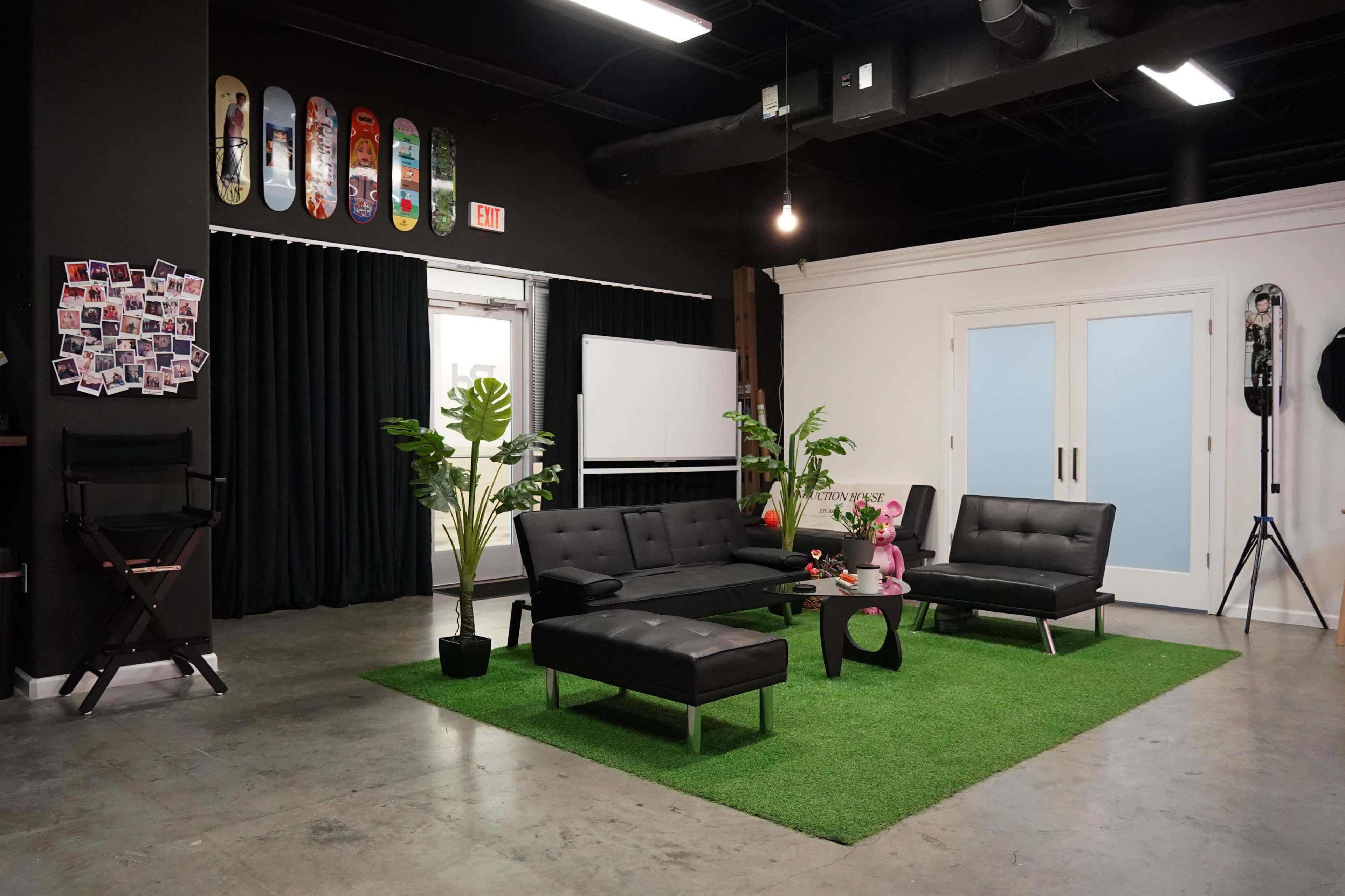 The room features a modern sitting area with black furniture arranged on green turf, surrounded by plants and adorned with skateboard art on the walls.