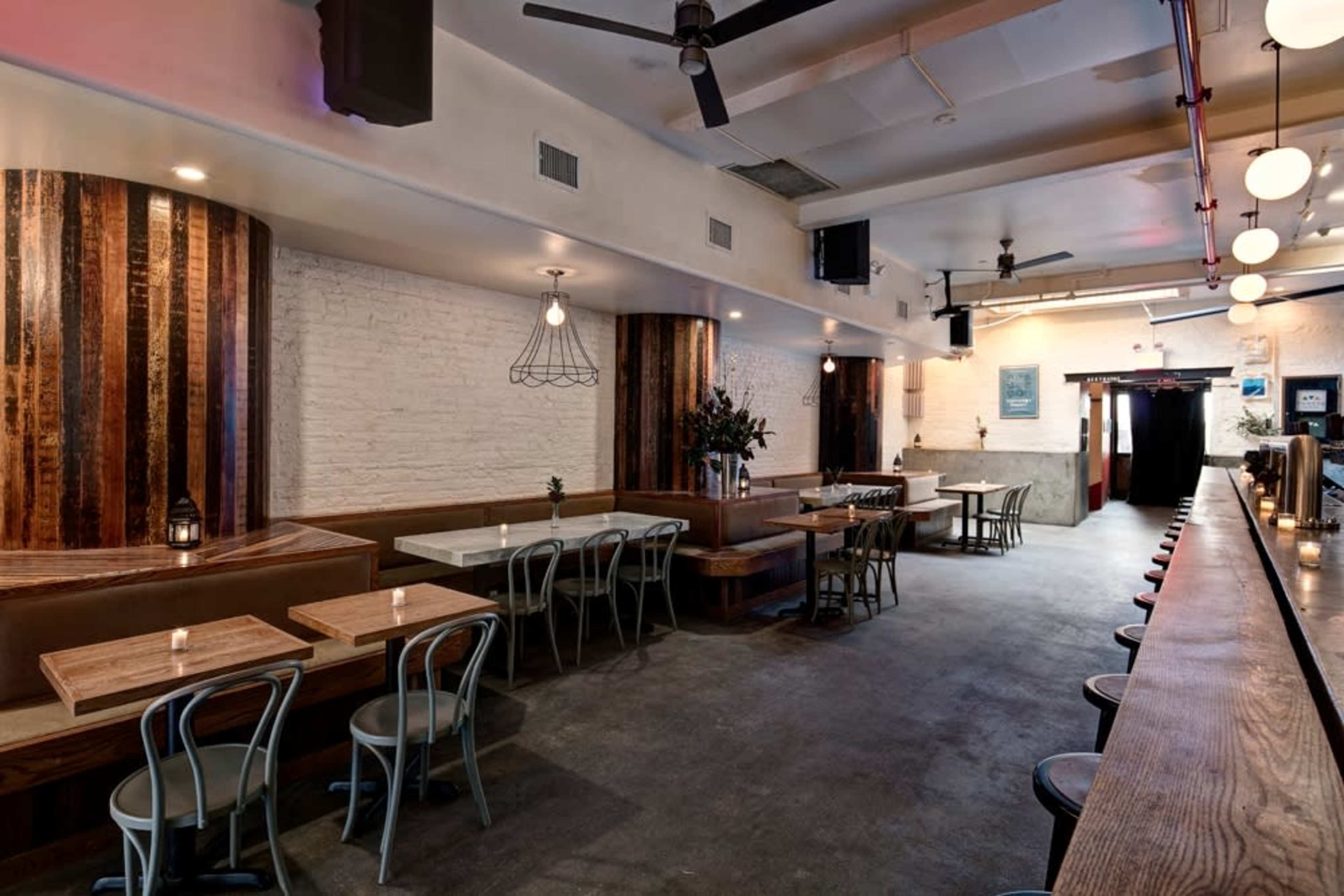 The image shows a spacious, modern indoor dining area featuring wooden seating, pendant lighting, and a long bar along one side.