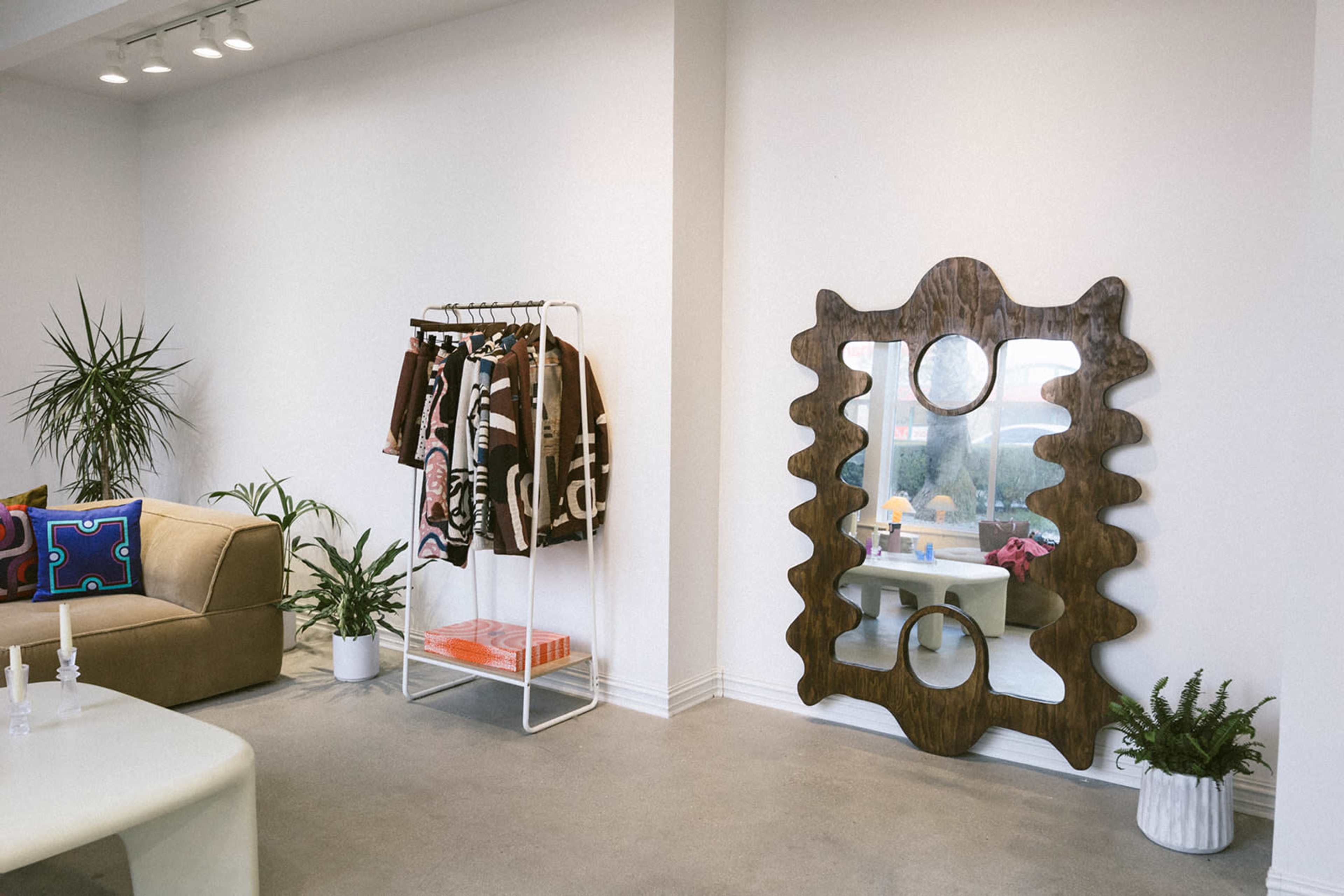 A modern interior with a clothing rack, a large decorative mirror, a sofa, and potted plants.