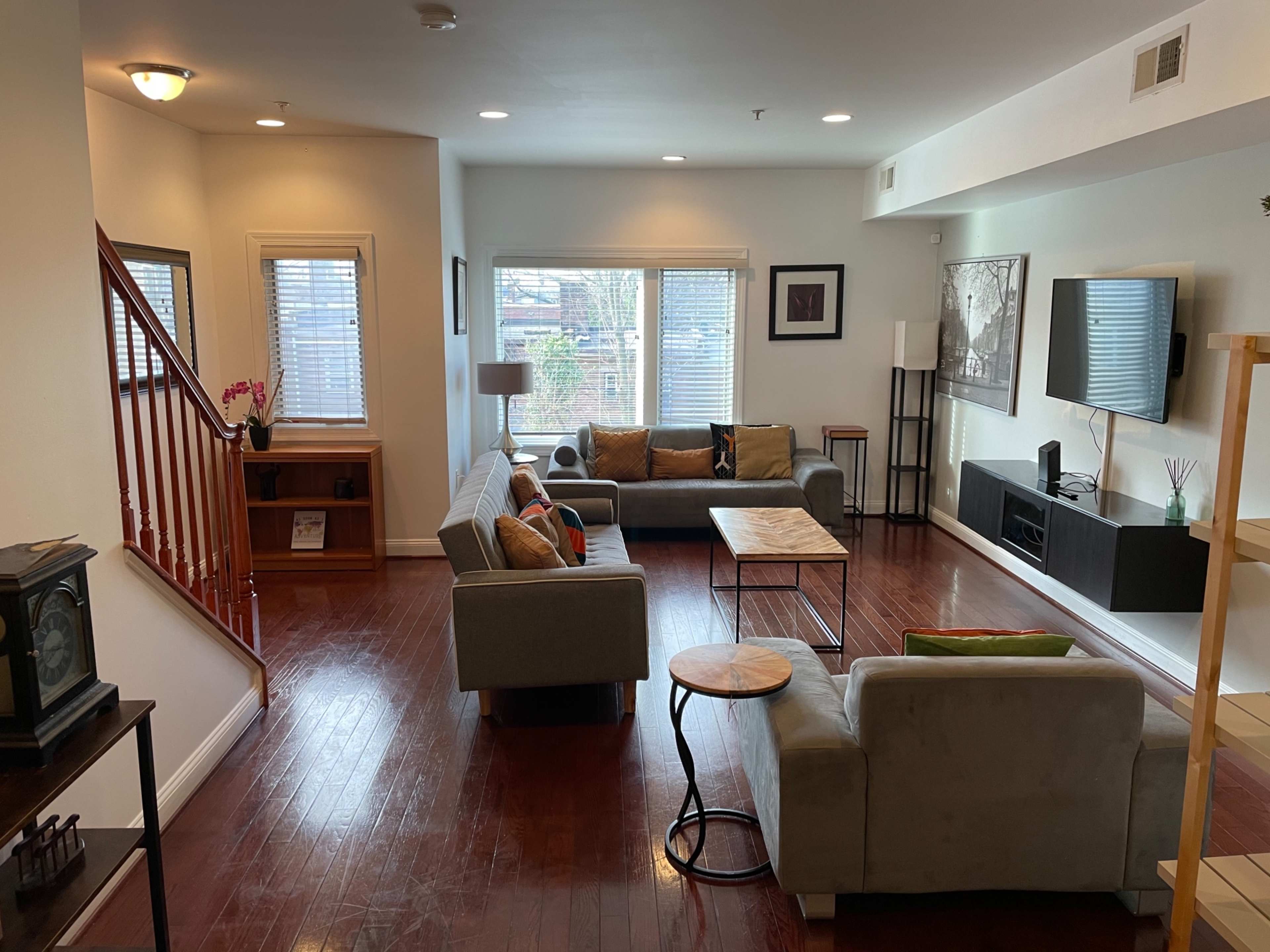 A living room with a staircase, two sofas, a wooden coffee table, and large windows allowing natural light.