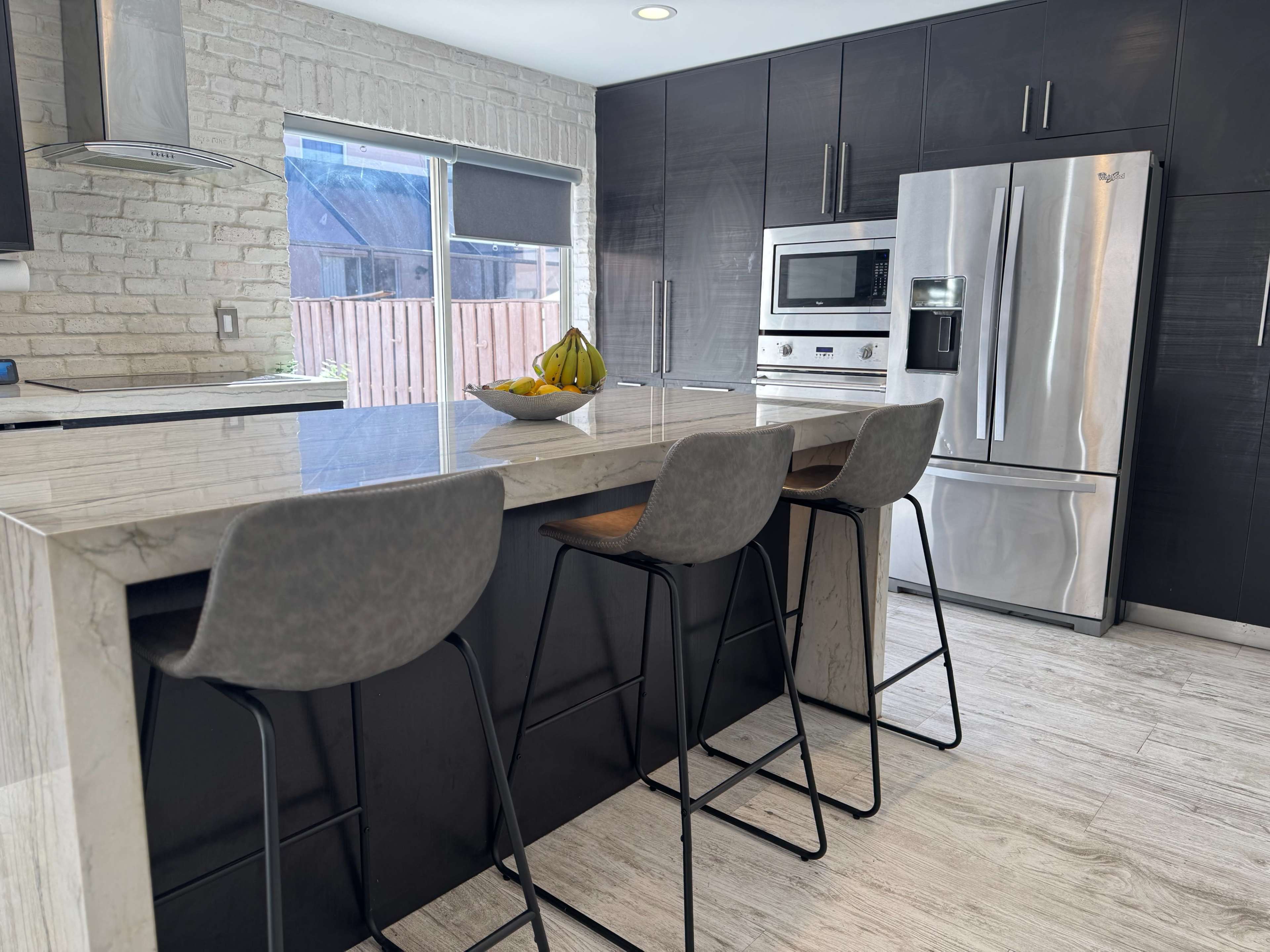 A modern kitchen features a marble countertop island with three stools and stainless steel appliances.