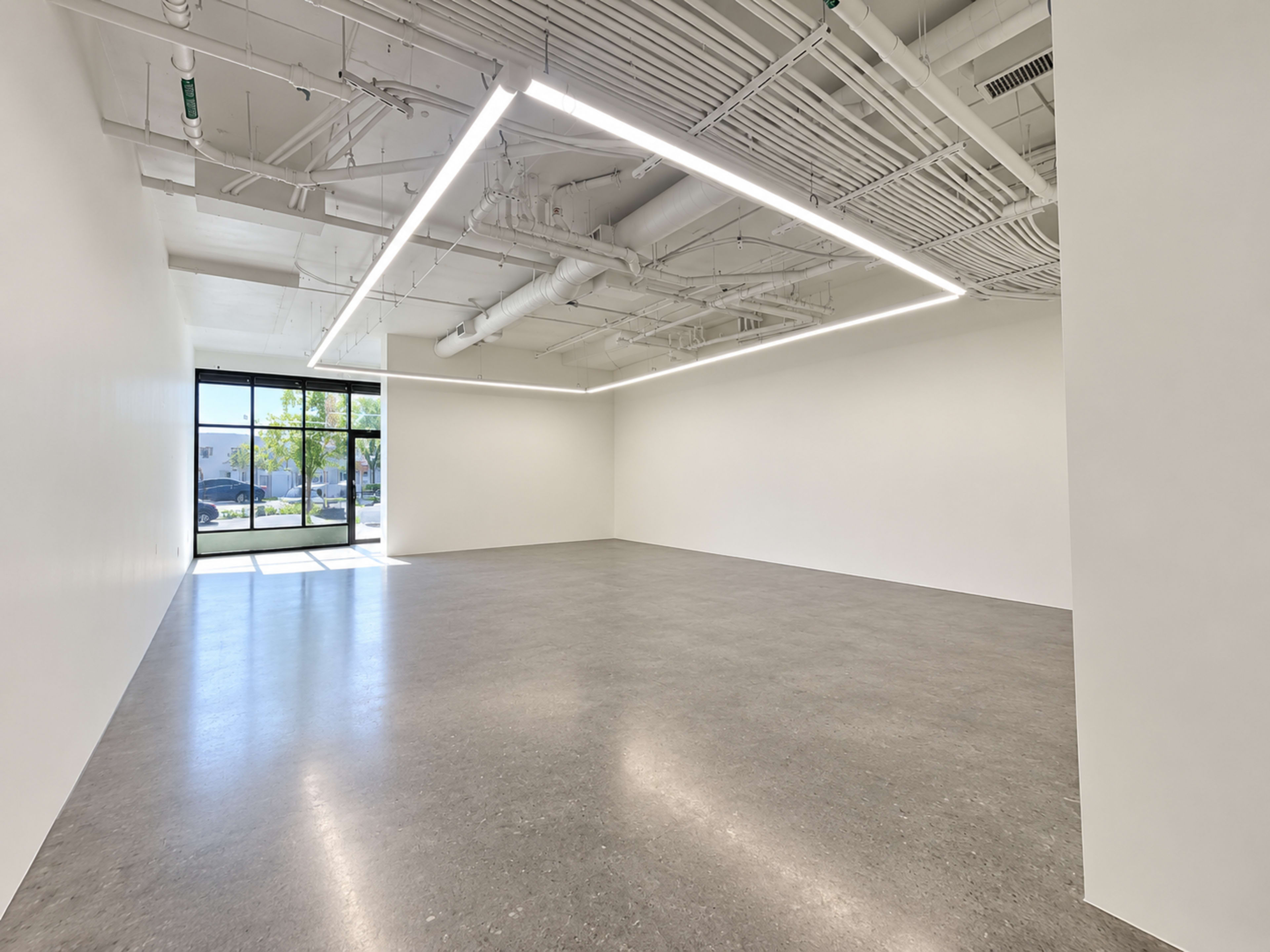 The image depicts a spacious, empty room with white walls and a large window allowing natural light to enter.