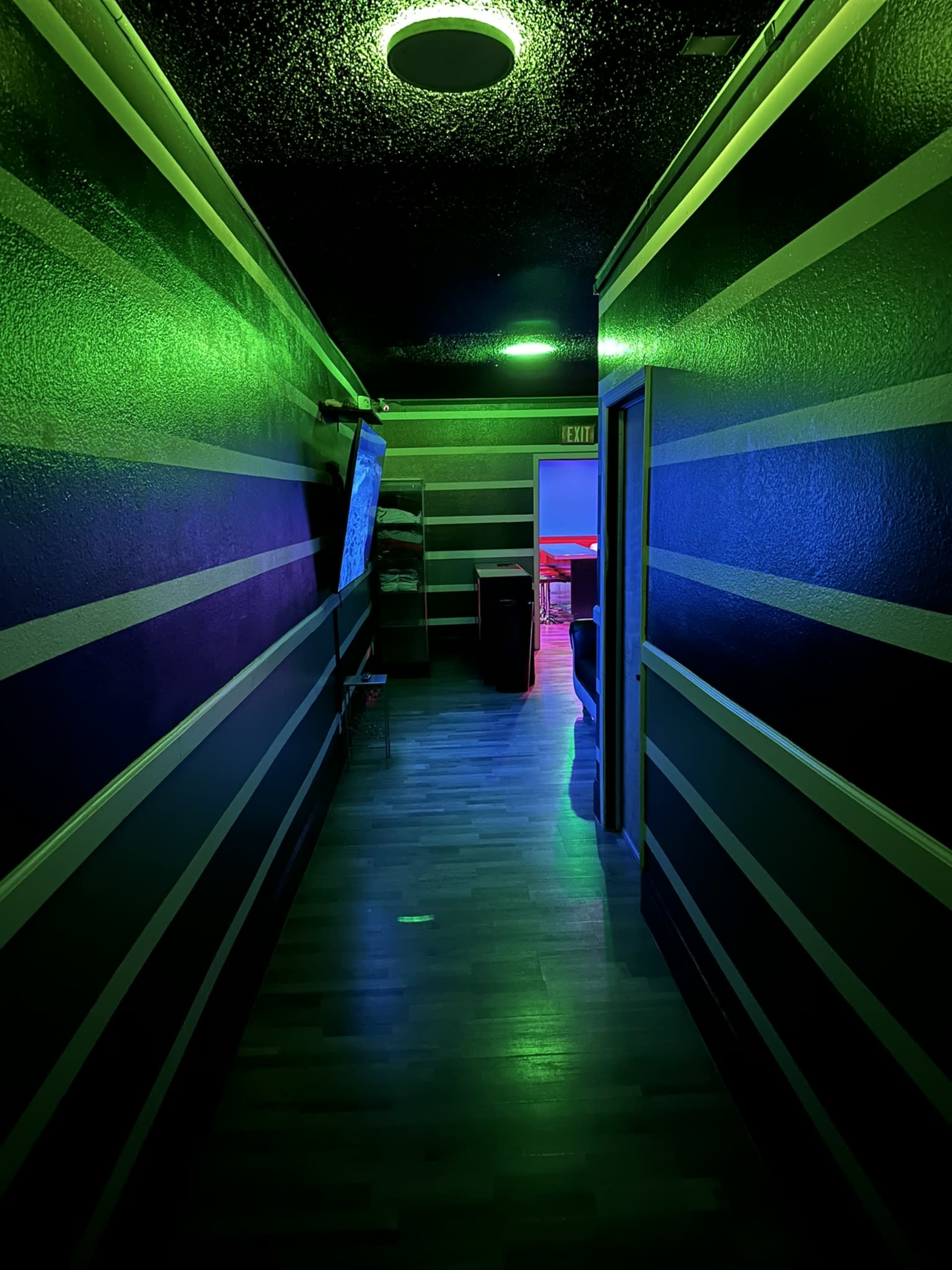A dimly lit hallway features striped walls in green and blue, leading to an exit door and a visible room at the end.