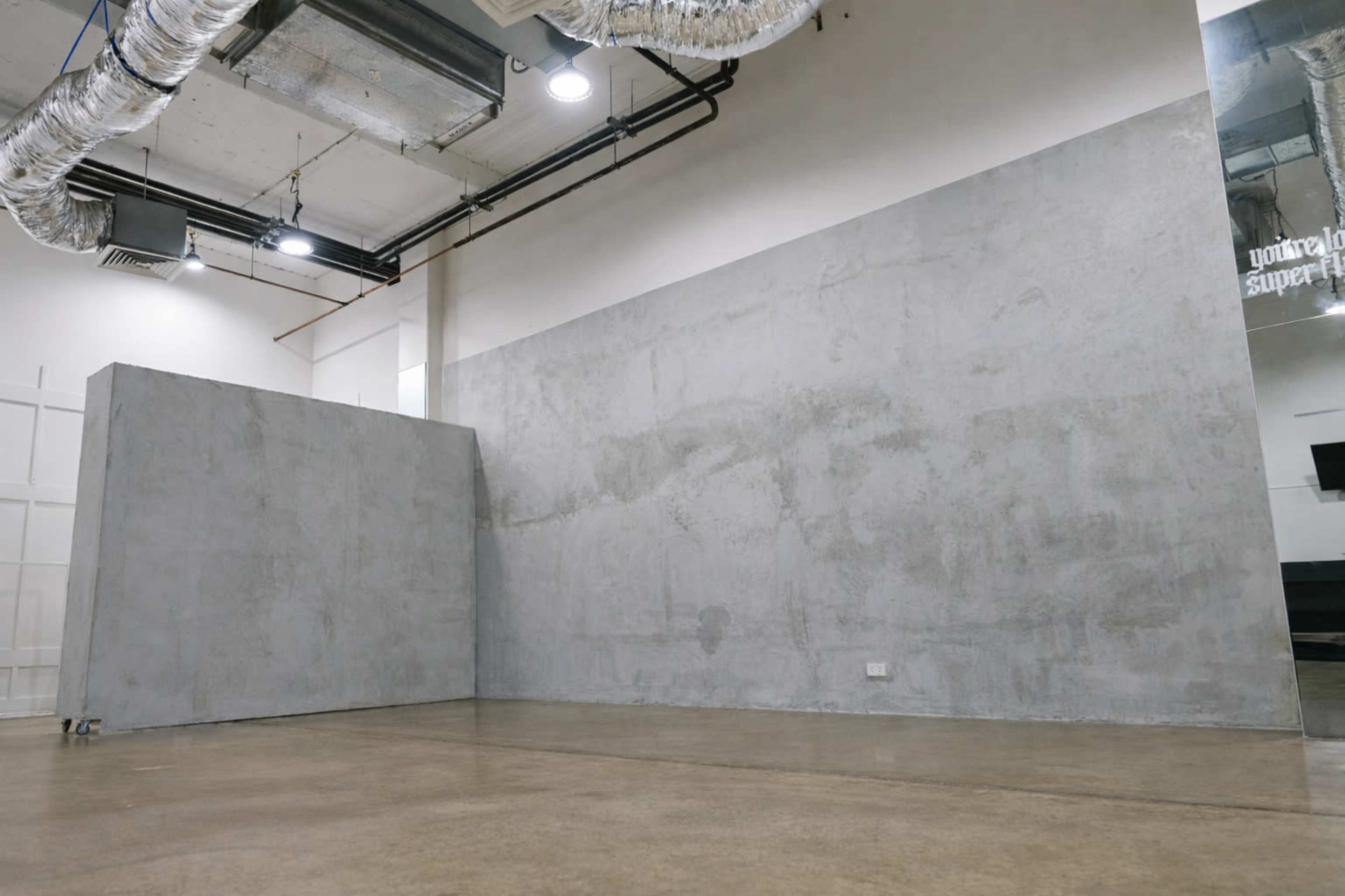 The image shows an industrial-style interior with bare concrete walls and a polished concrete floor, featuring exposed ductwork above.