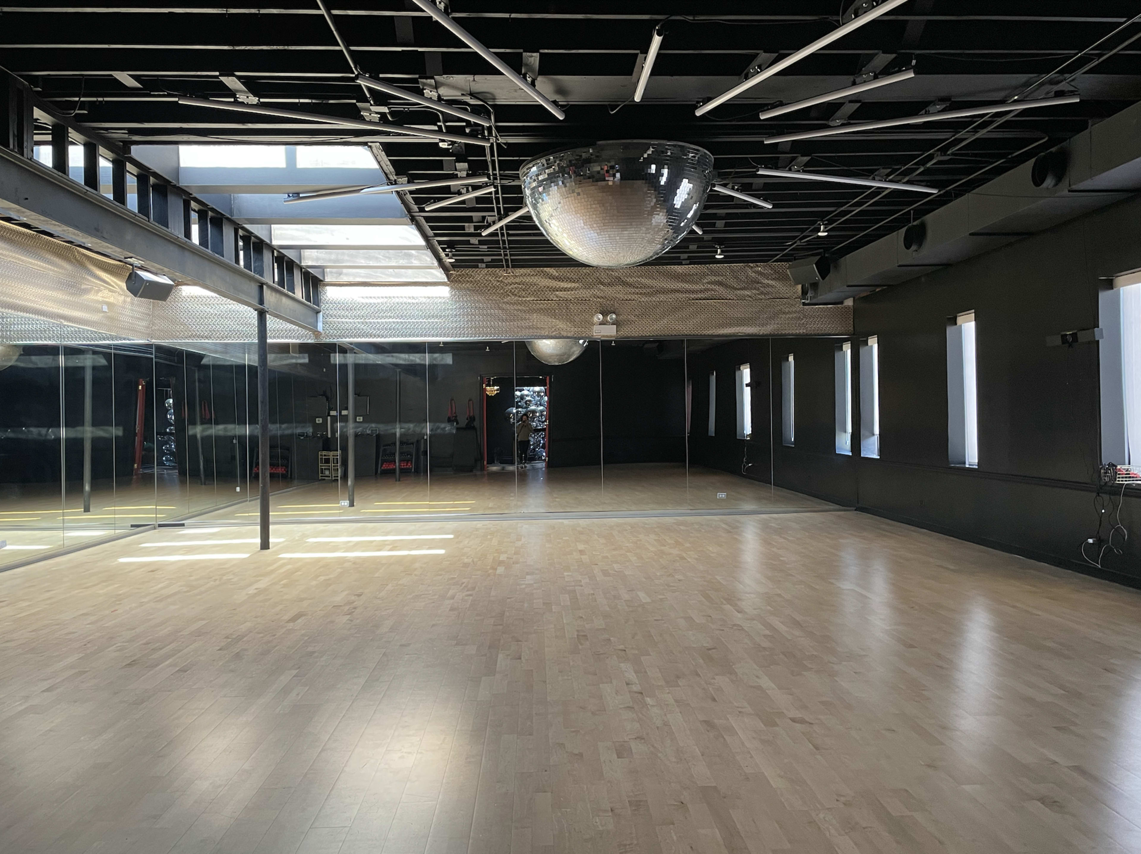A spacious dance studio with wooden flooring, large mirrors on one wall, and a disco ball hanging from the ceiling.