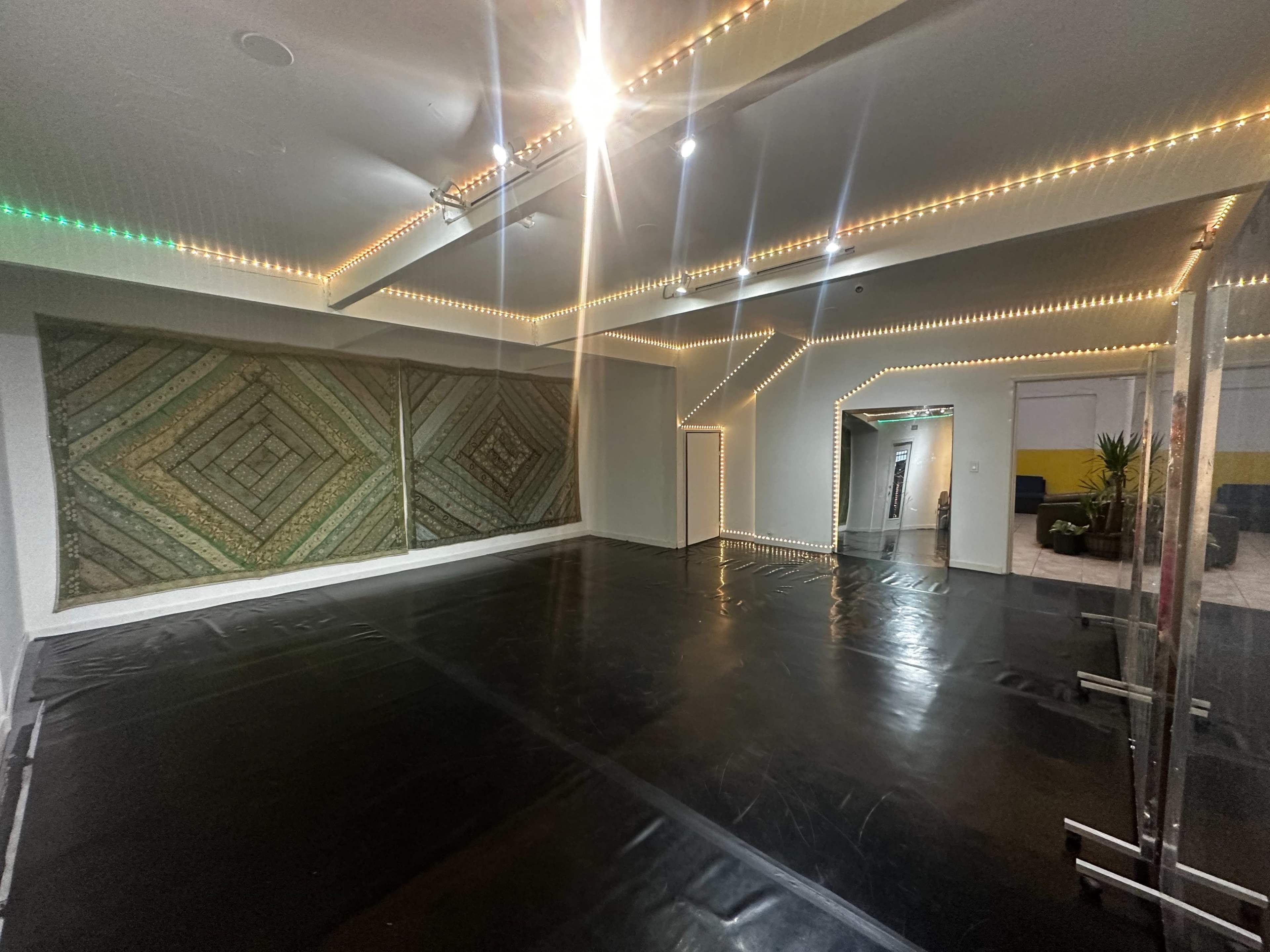 The image shows a spacious room with a black floor, illuminated by LED lights along the walls and featuring a large patterned wall hanging.