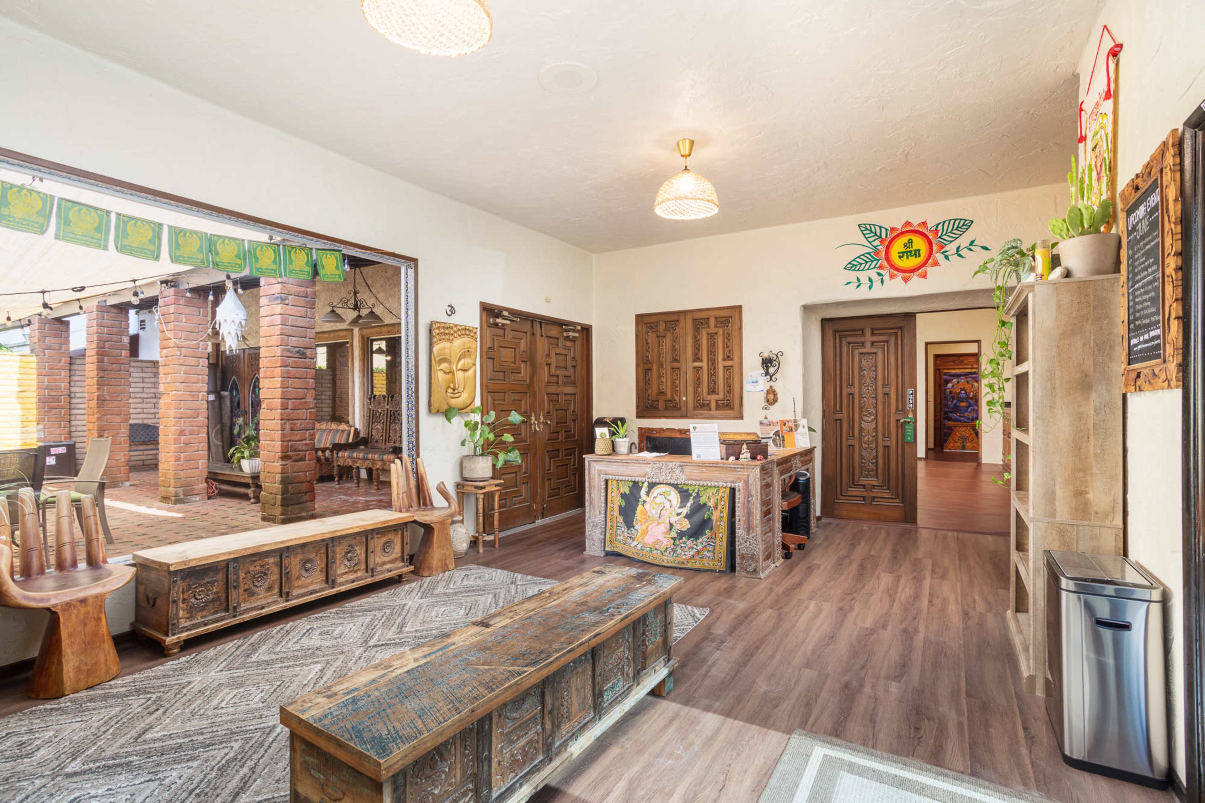 The image shows a spacious, well-decorated reception area featuring wooden furniture, plants, and artwork, with a view leading to an outdoor courtyard.