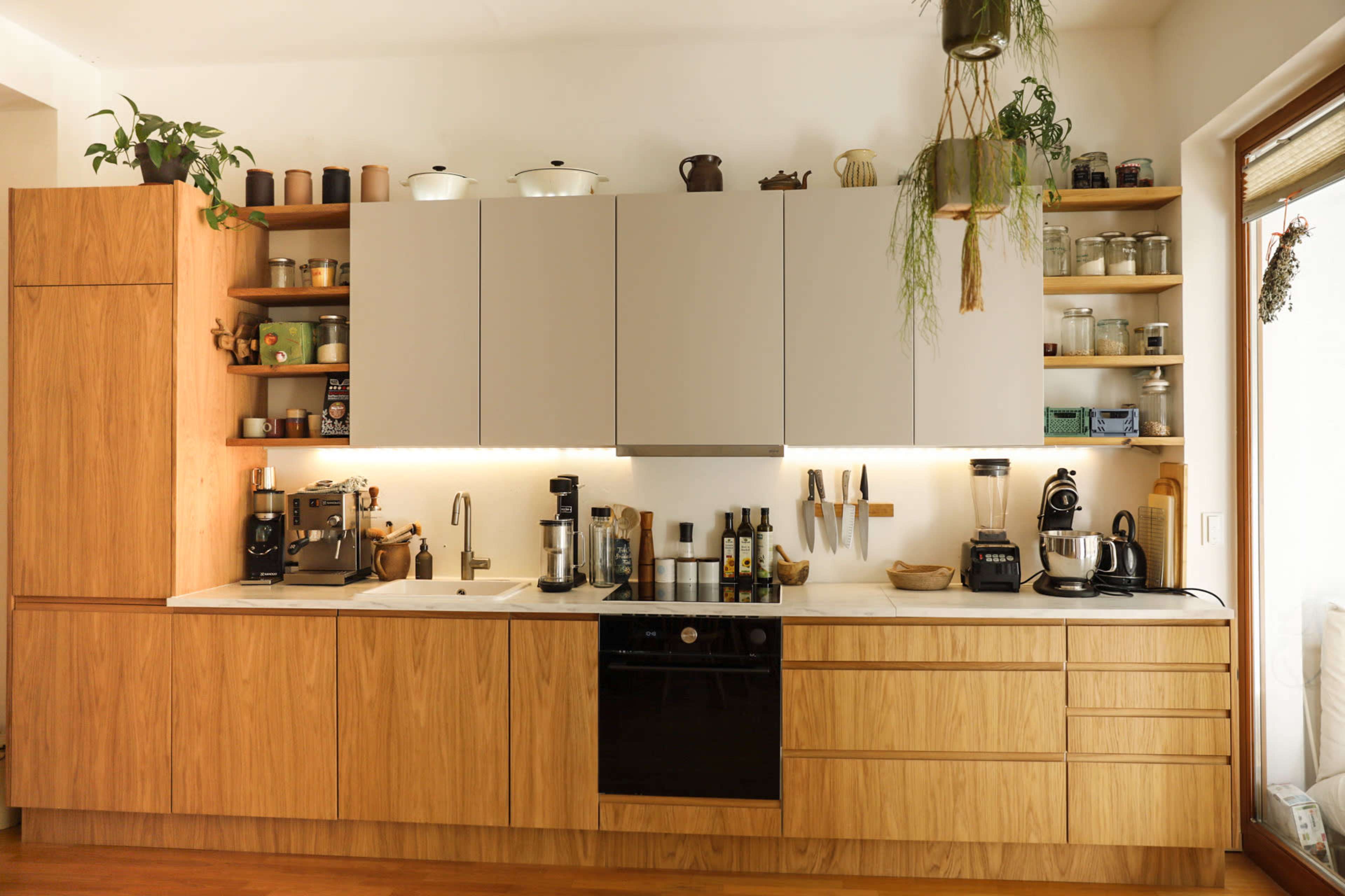 The image shows a modern kitchen with wooden cabinetry, a black dishwasher, and various kitchen appliances neatly arranged on the countertop.