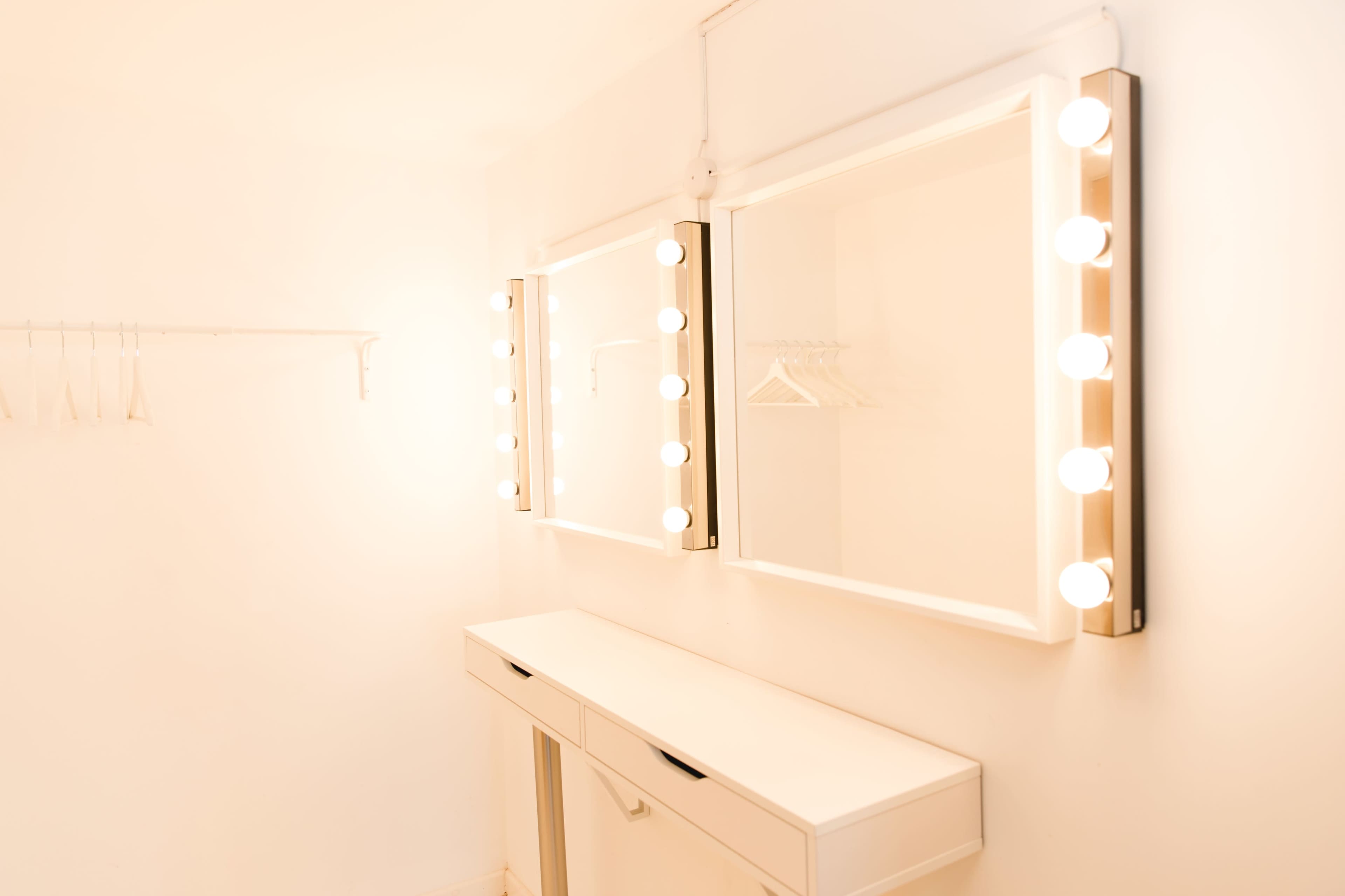 A well-lit dressing room with two mirrors framed by lightbulbs and a white vanity below them.