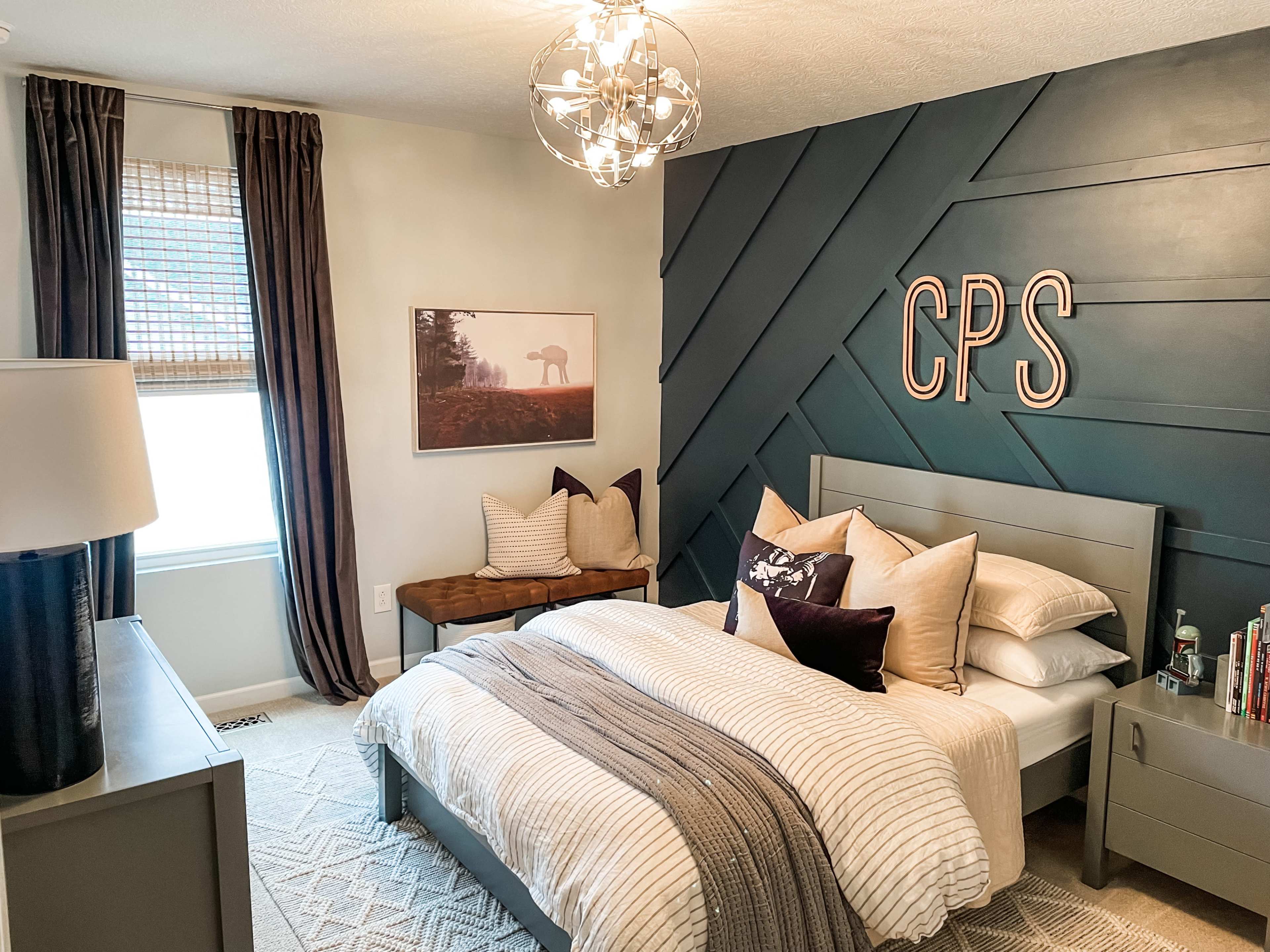 A modern bedroom featuring a gray bed with decorative pillows, a dark accent wall with "CPS" letters, and a large window with light curtains.
