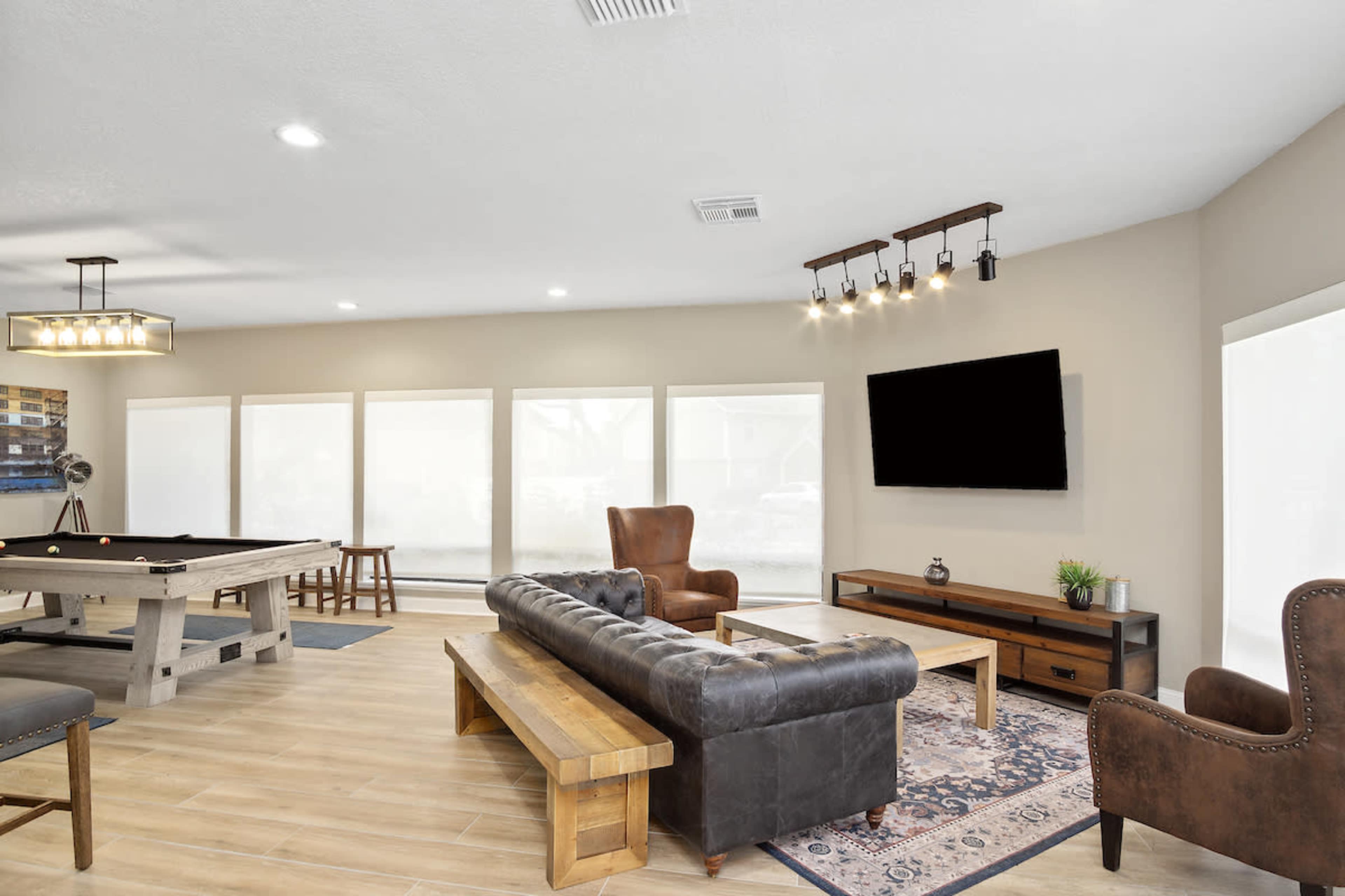 A spacious game room featuring a pool table, a leather sofa, armchairs, and a television mounted on the wall.