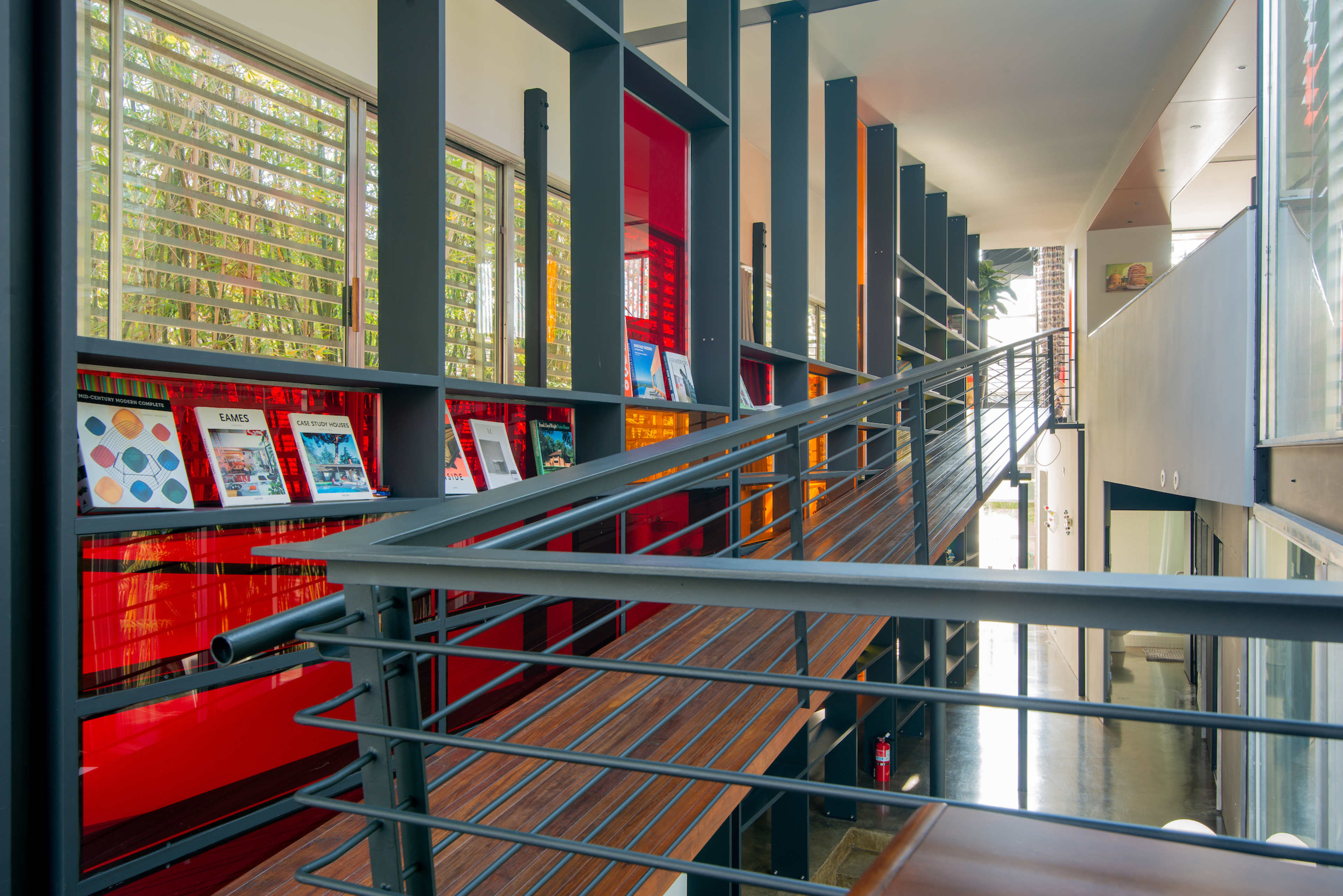 A modern interior space featuring a staircase with metal railings, wooden treads, and a wall displaying framed items against a bright red backdrop.