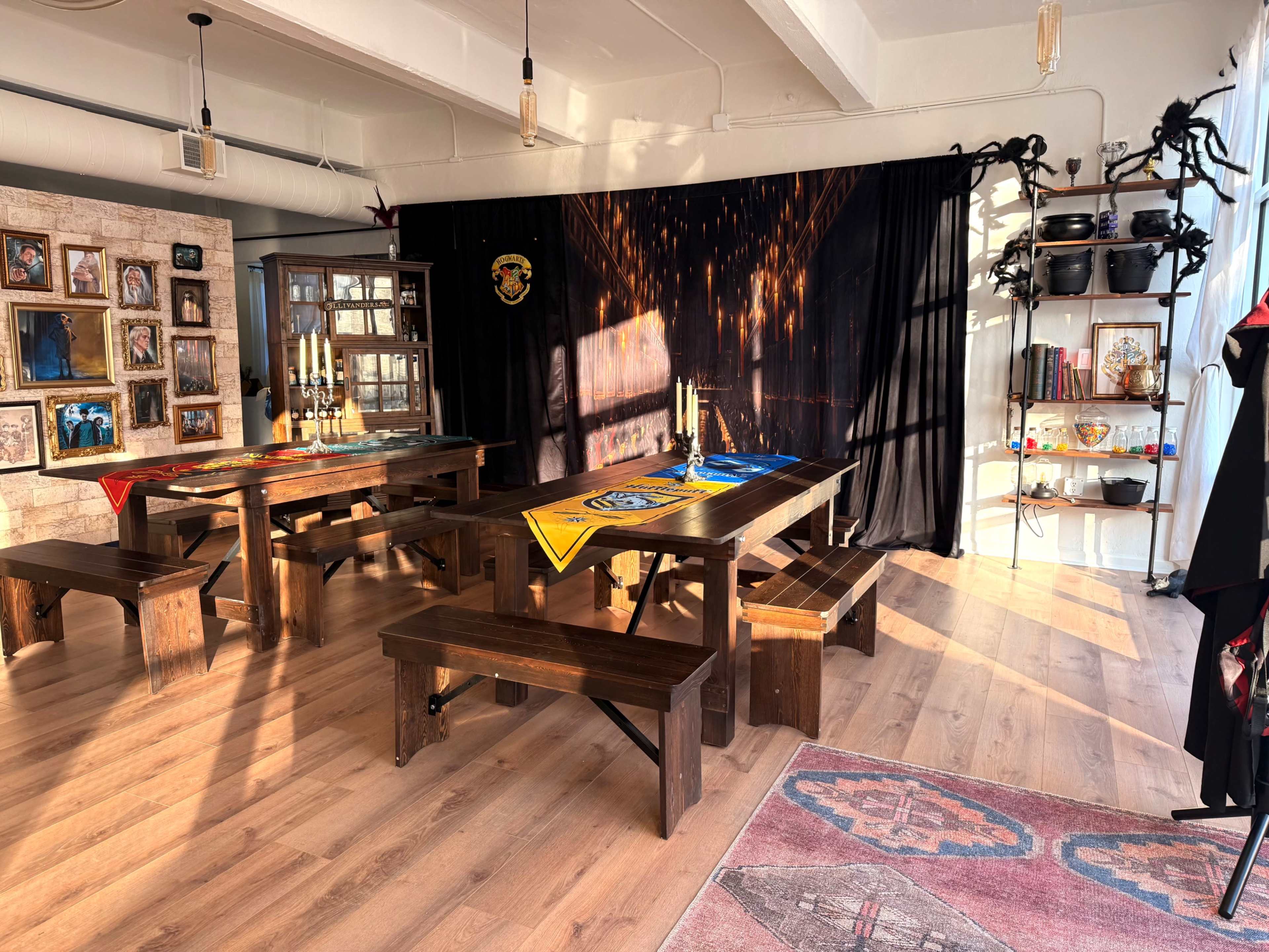 The room features a long wooden table and benches, adorned with colorful tablecloths, surrounded by walls displaying framed photos and shelves filled with decorative items.