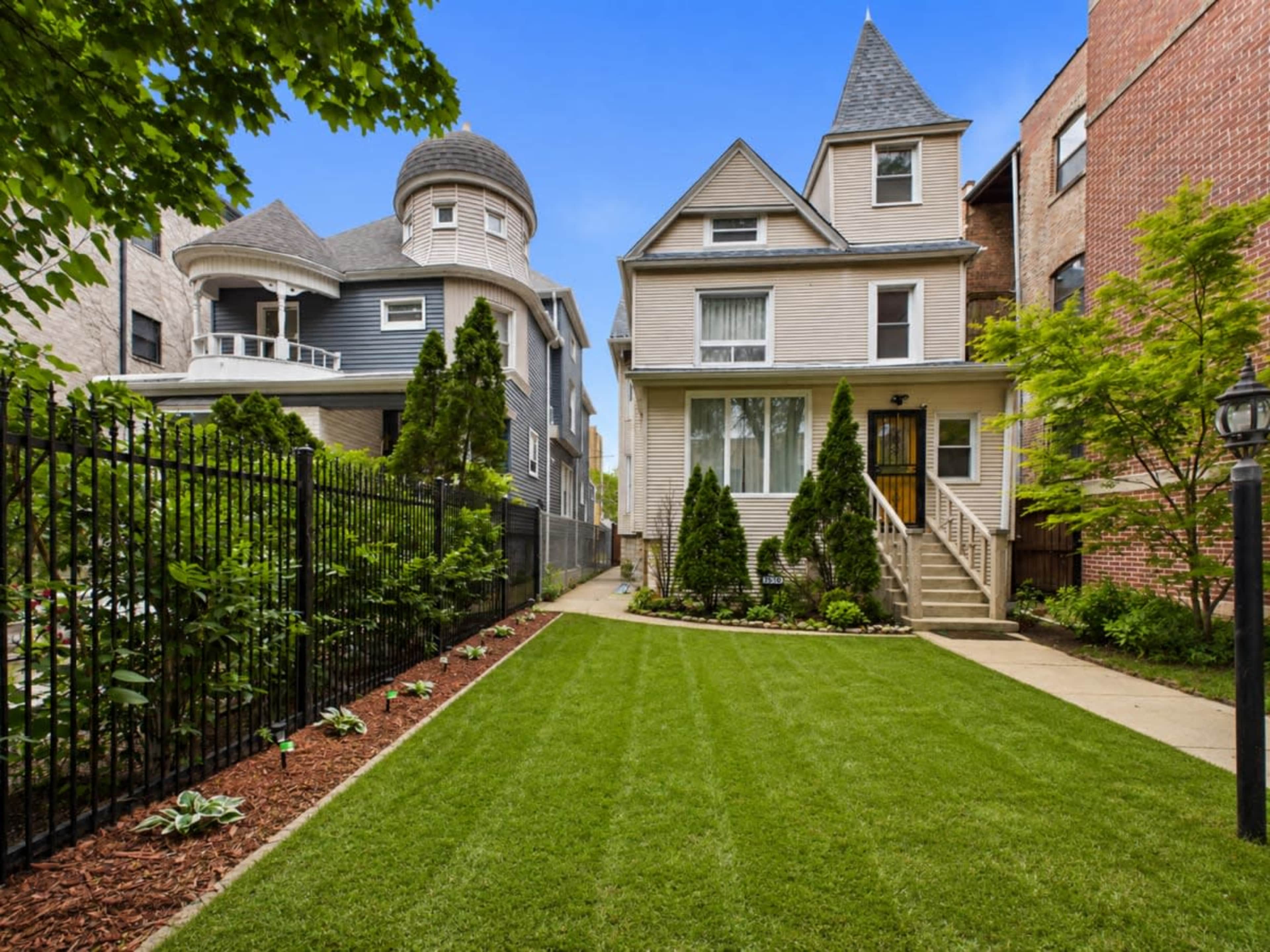 The image shows a well-maintained residential property with a manicured lawn and two distinct architectural styles of neighboring houses.