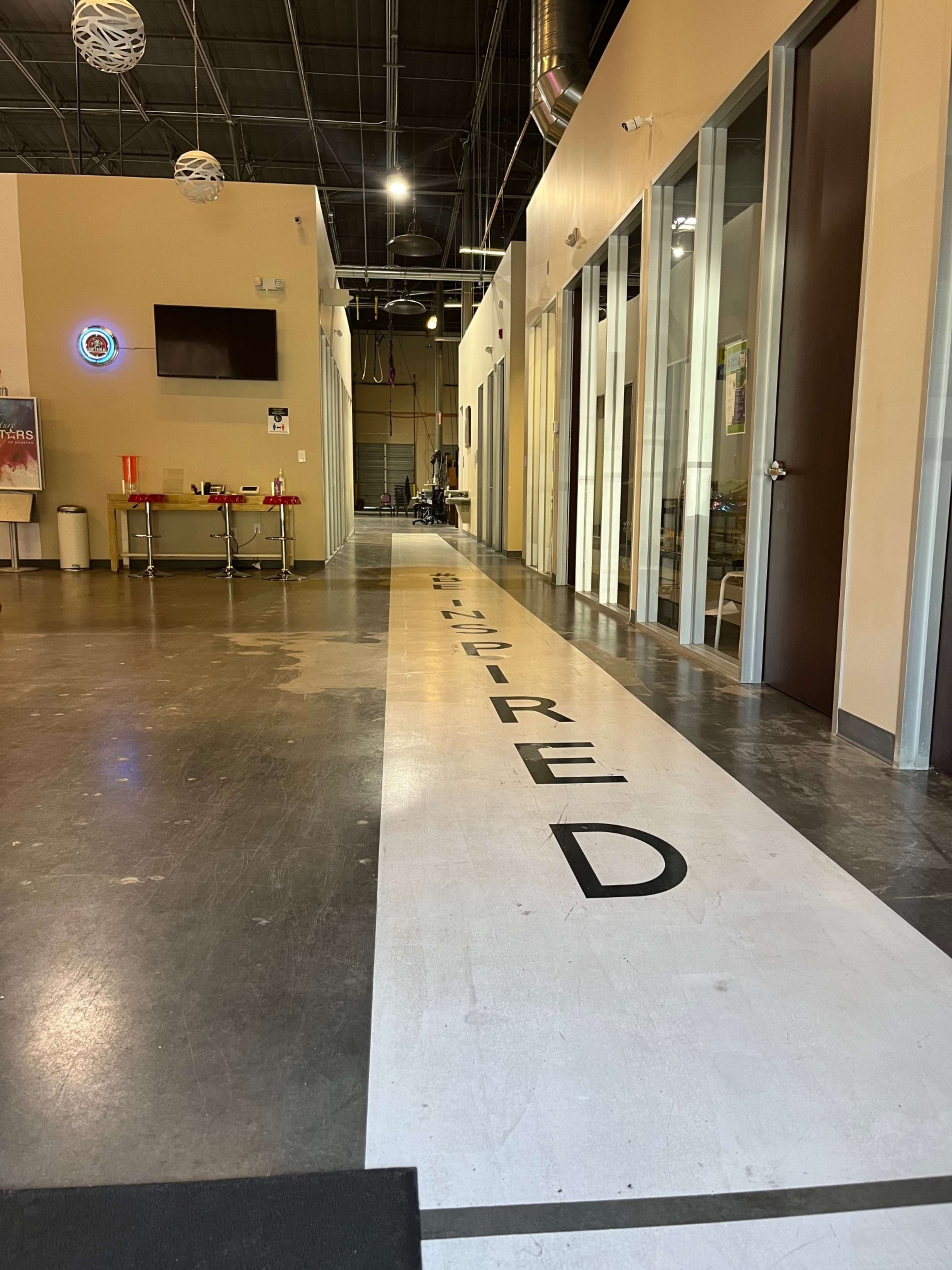 A corridor with the word "INSPIRED" prominently displayed on the floor, leading towards several doorways and a seating area.