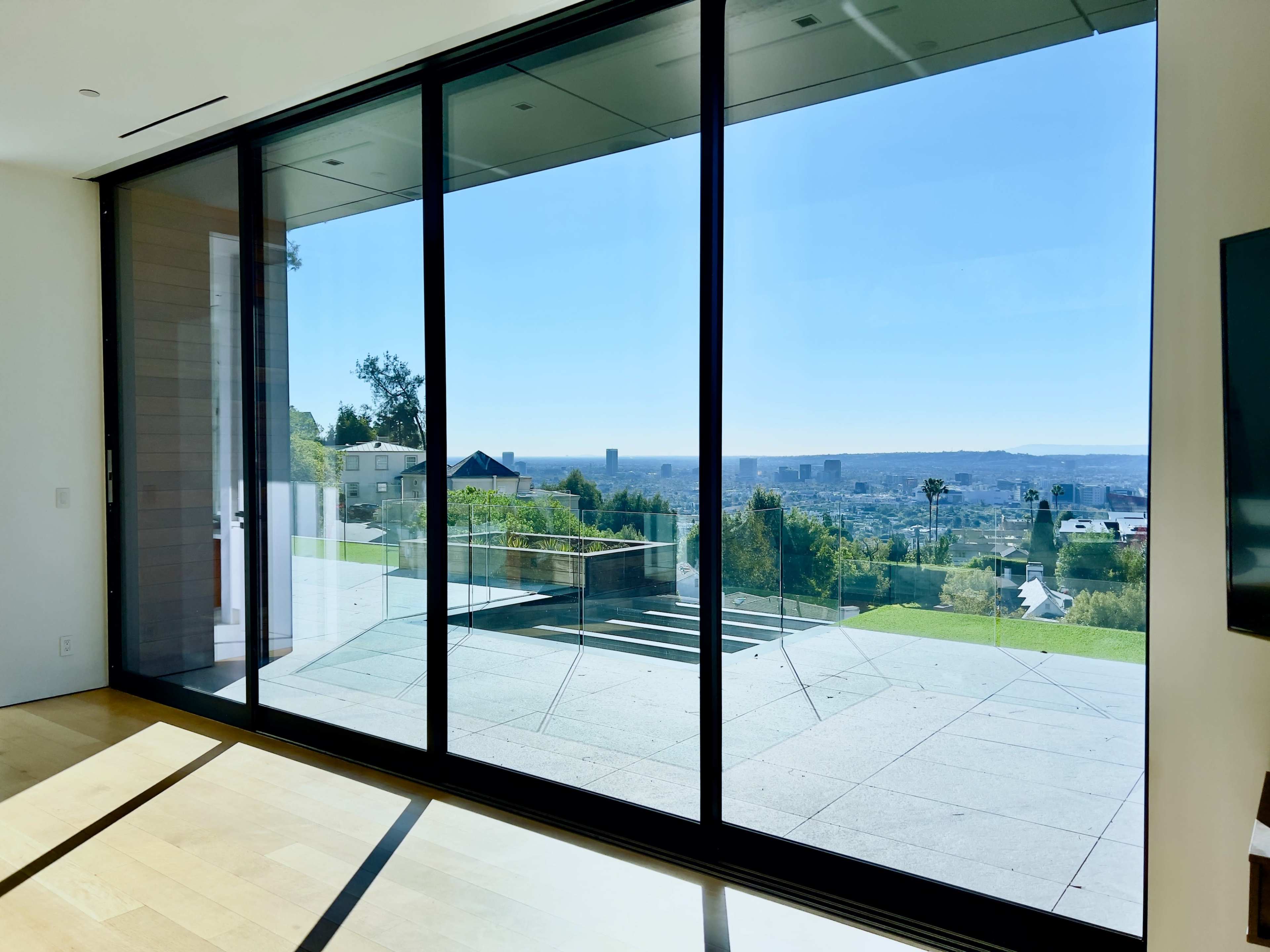 The image shows a modern interior with large glass doors opening onto a patio and a view of a city skyline.