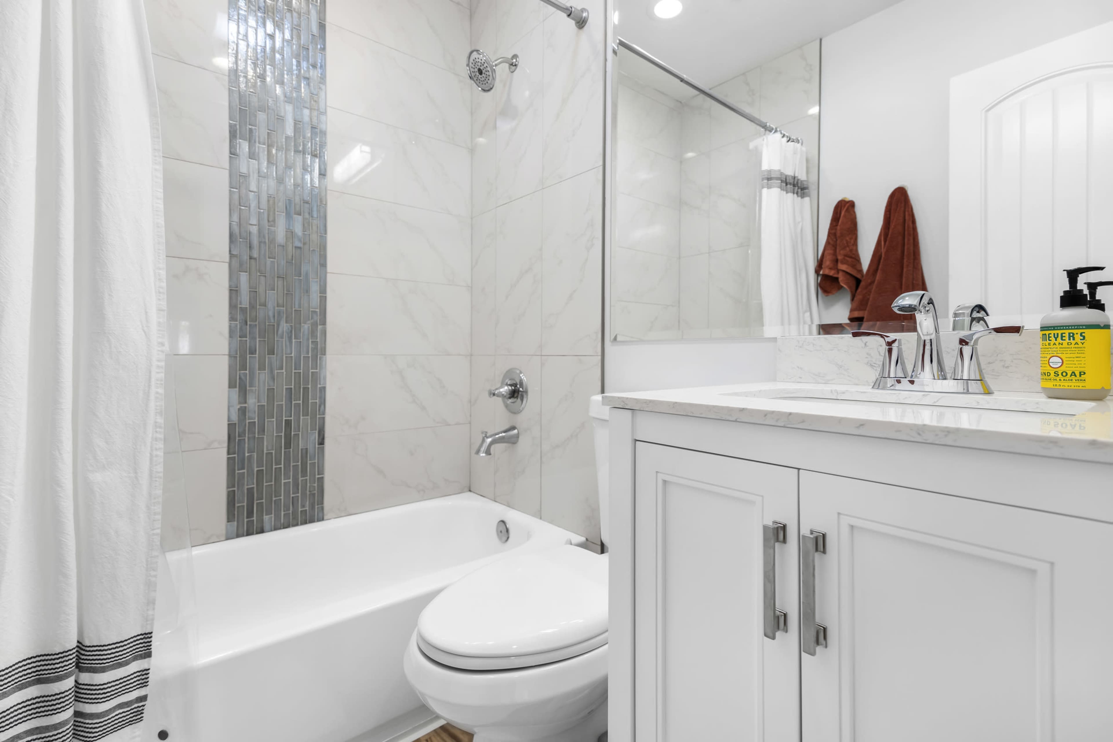The image shows a modern bathroom featuring a bathtub with a glass shower enclosure, a white vanity with a marble countertop, and tiled walls.