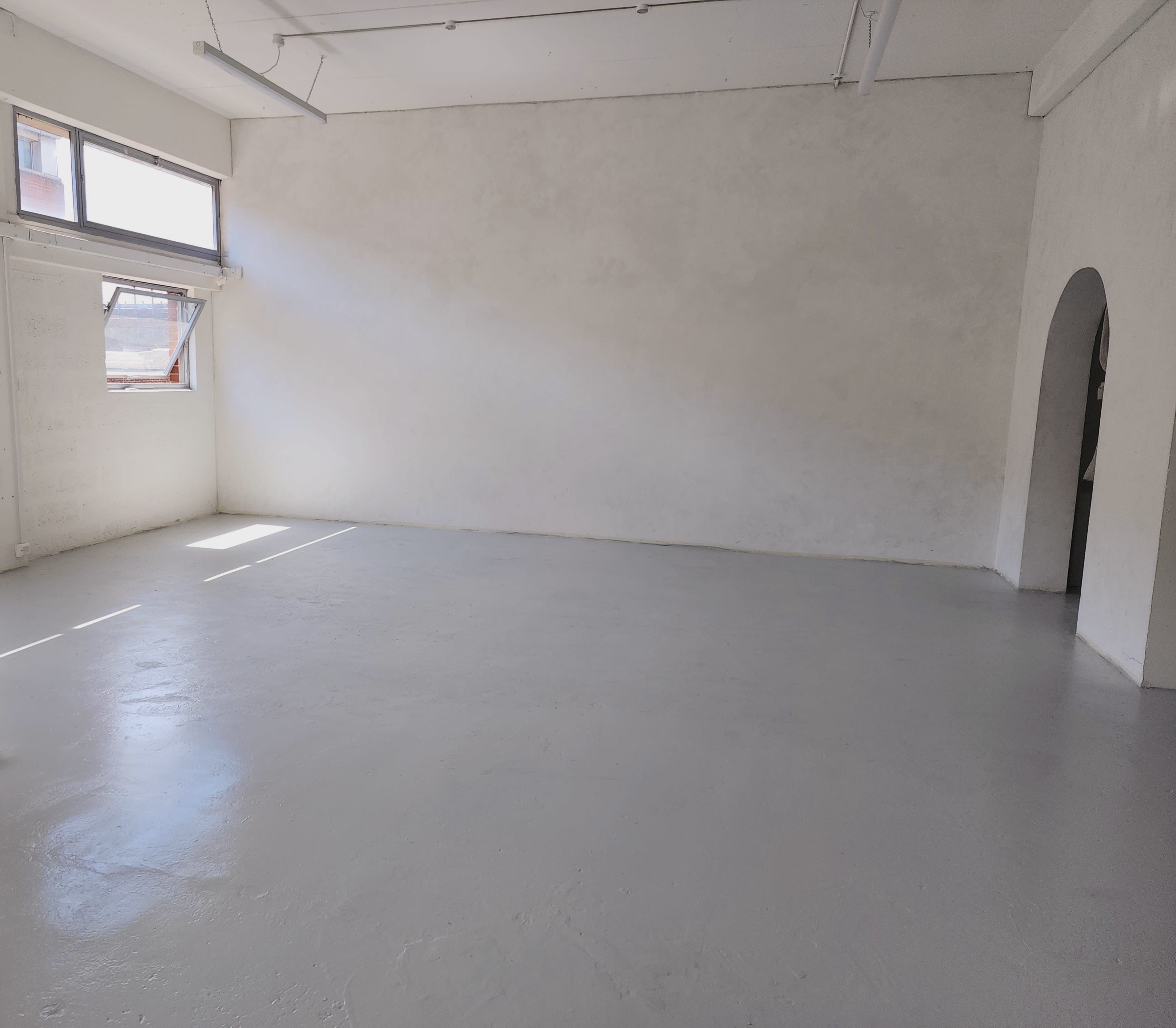 A spacious, empty room with a gray floor, white walls, and large windows allowing natural light.
