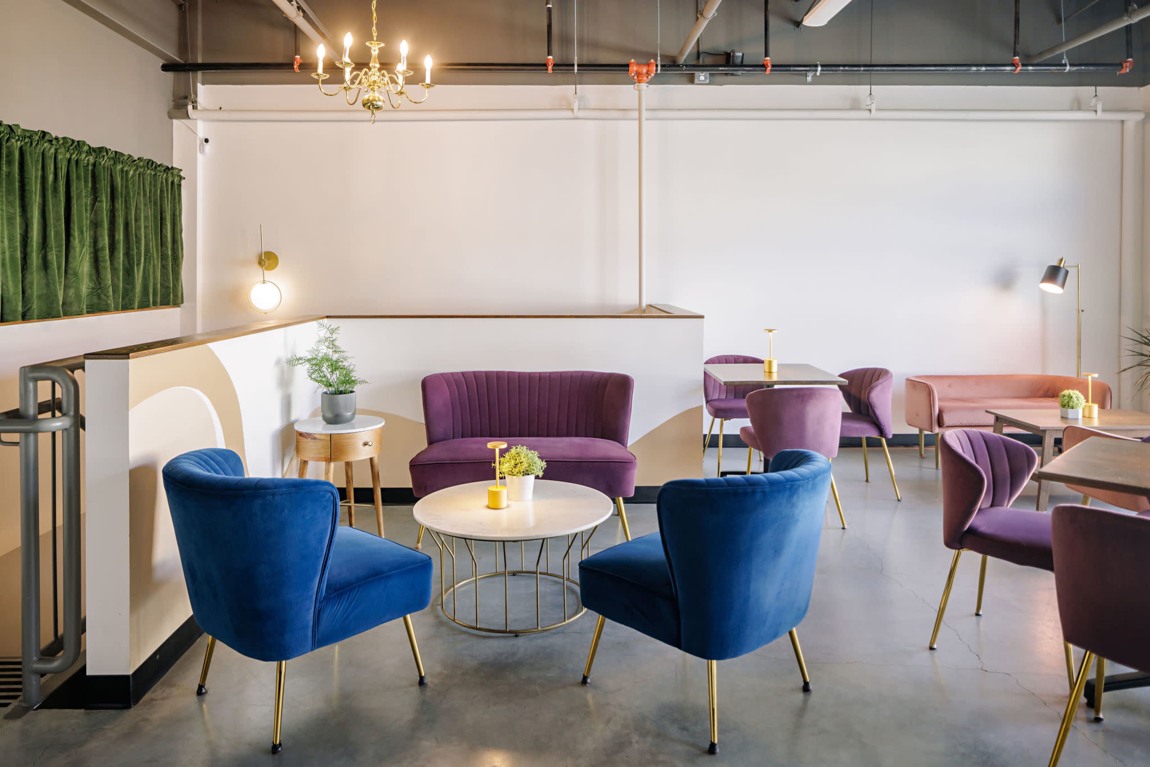 The image shows a modern lounge area with purple and blue upholstered chairs, a round table, and a small potted plant, set against a neutral wall and ceiling with industrial lighting.