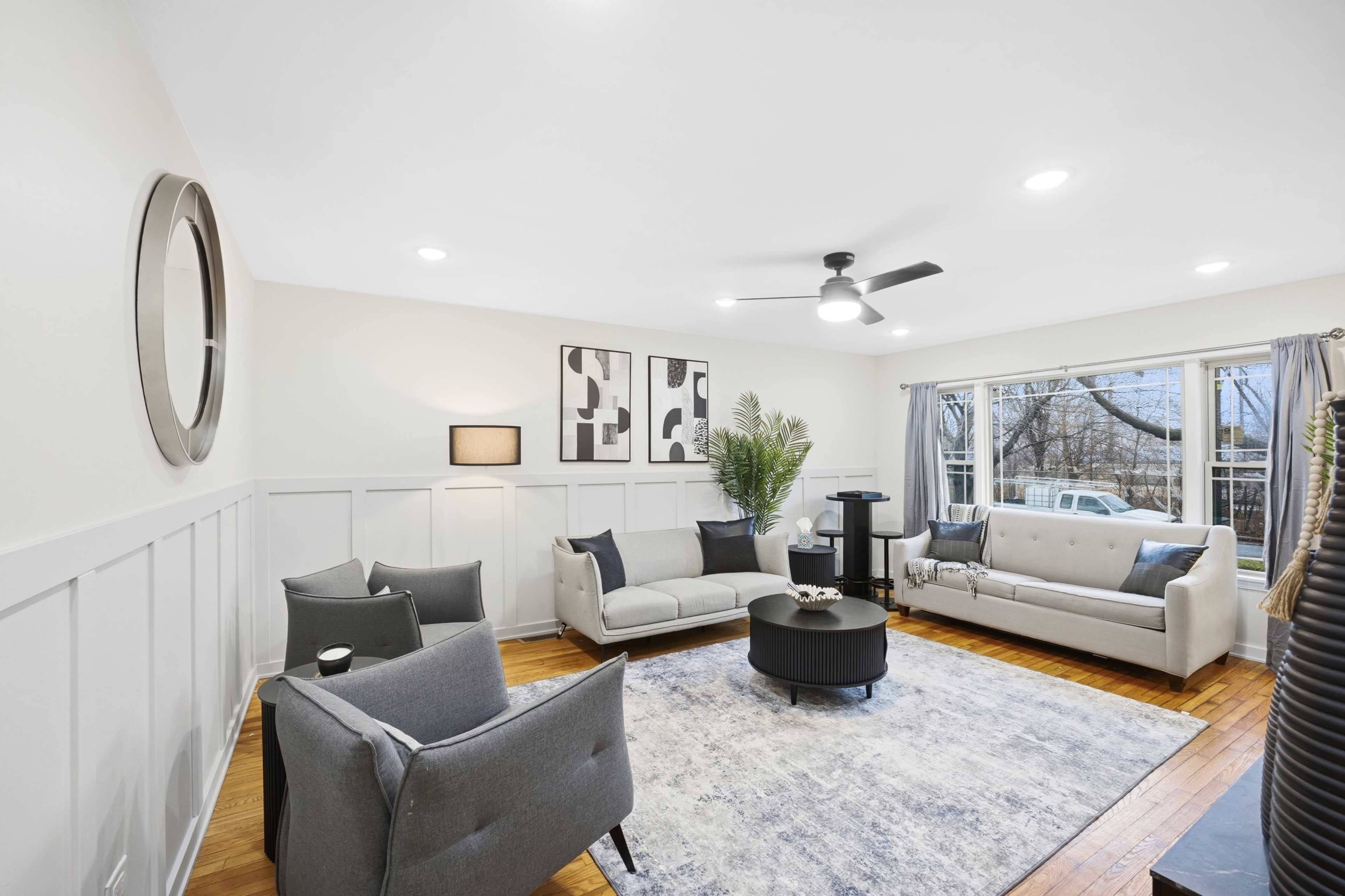 The image depicts a modern living room with a gray sectional sofa, a coffee table in the center, and large windows allowing natural light to enter.