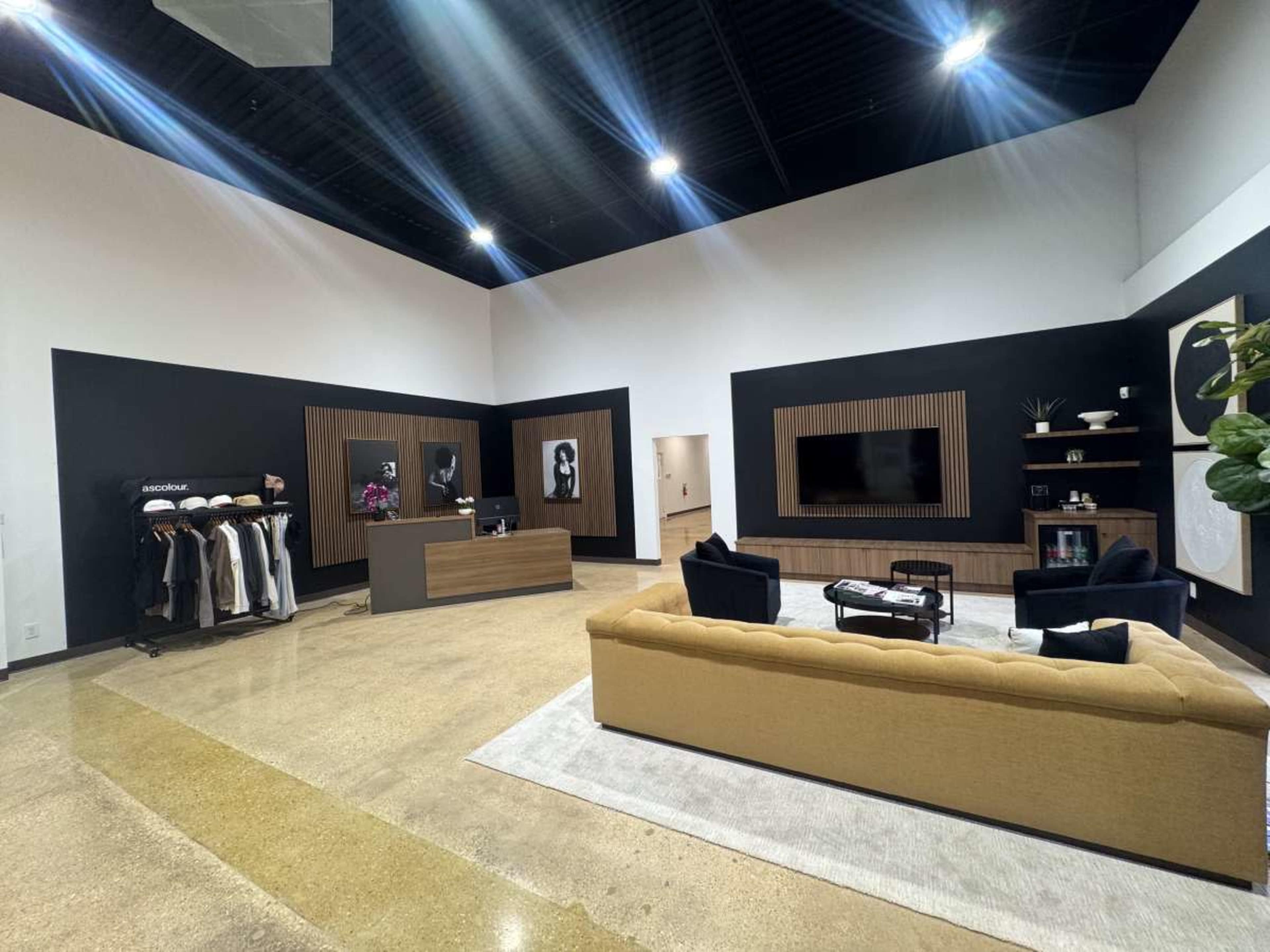 The image shows a modern office space with a reception area, featuring a beige sofa, a dark gray wall, and a clothing rack displaying various garments.