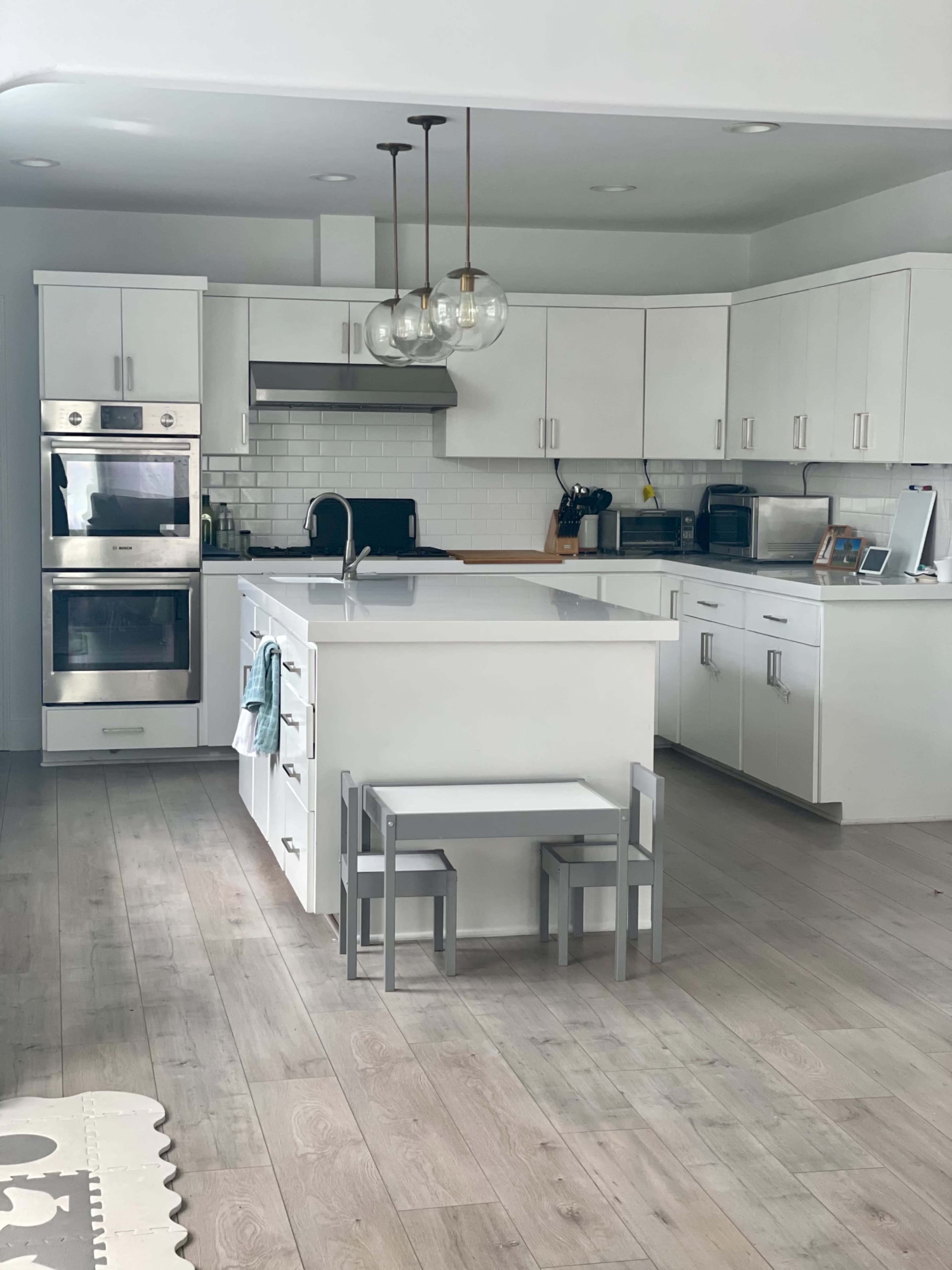 A modern kitchen features white cabinets, stainless steel appliances, and a central island with two small stools.